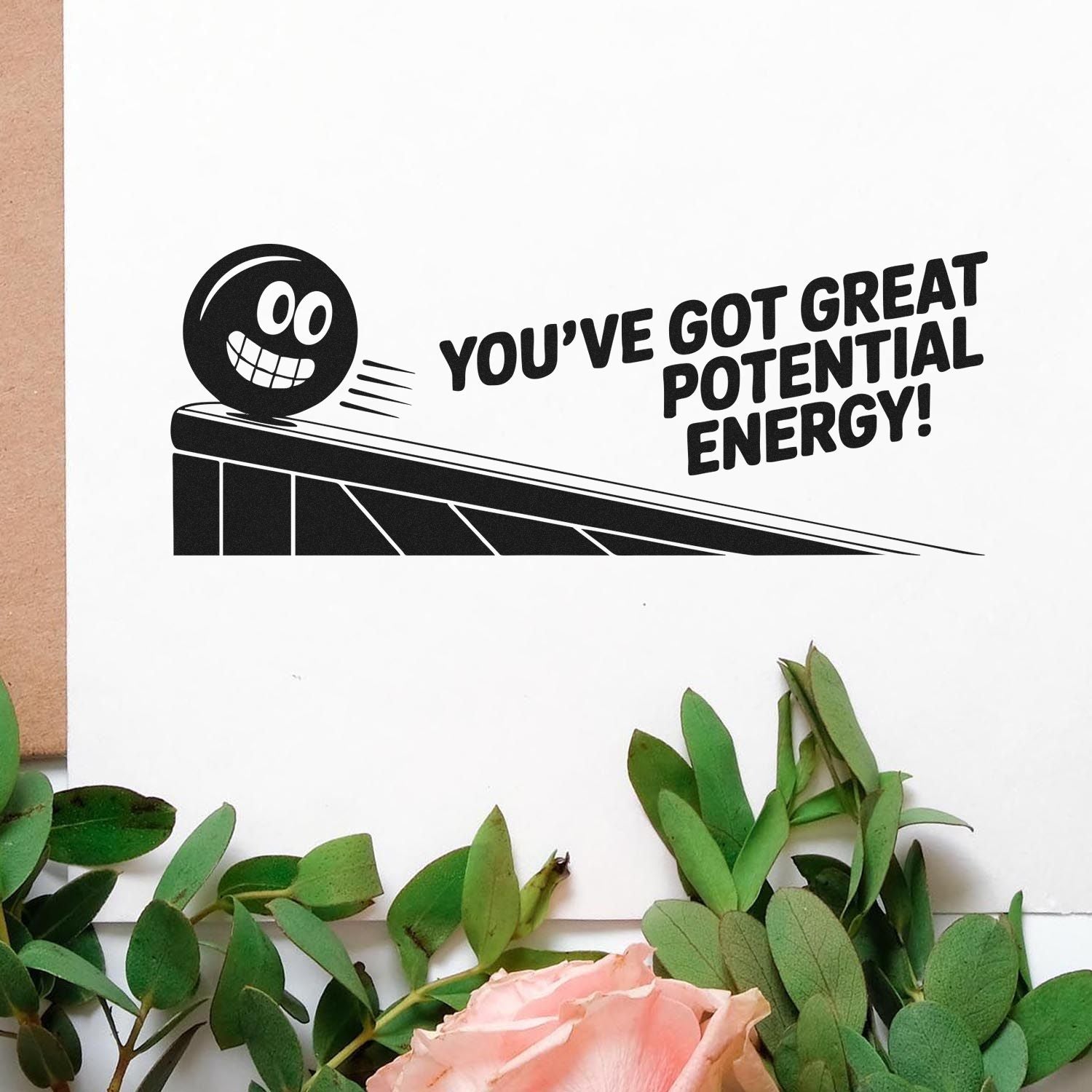 Black motivational stamp seal with smiling face and Youve got great potential energy! on white paper with greenery.