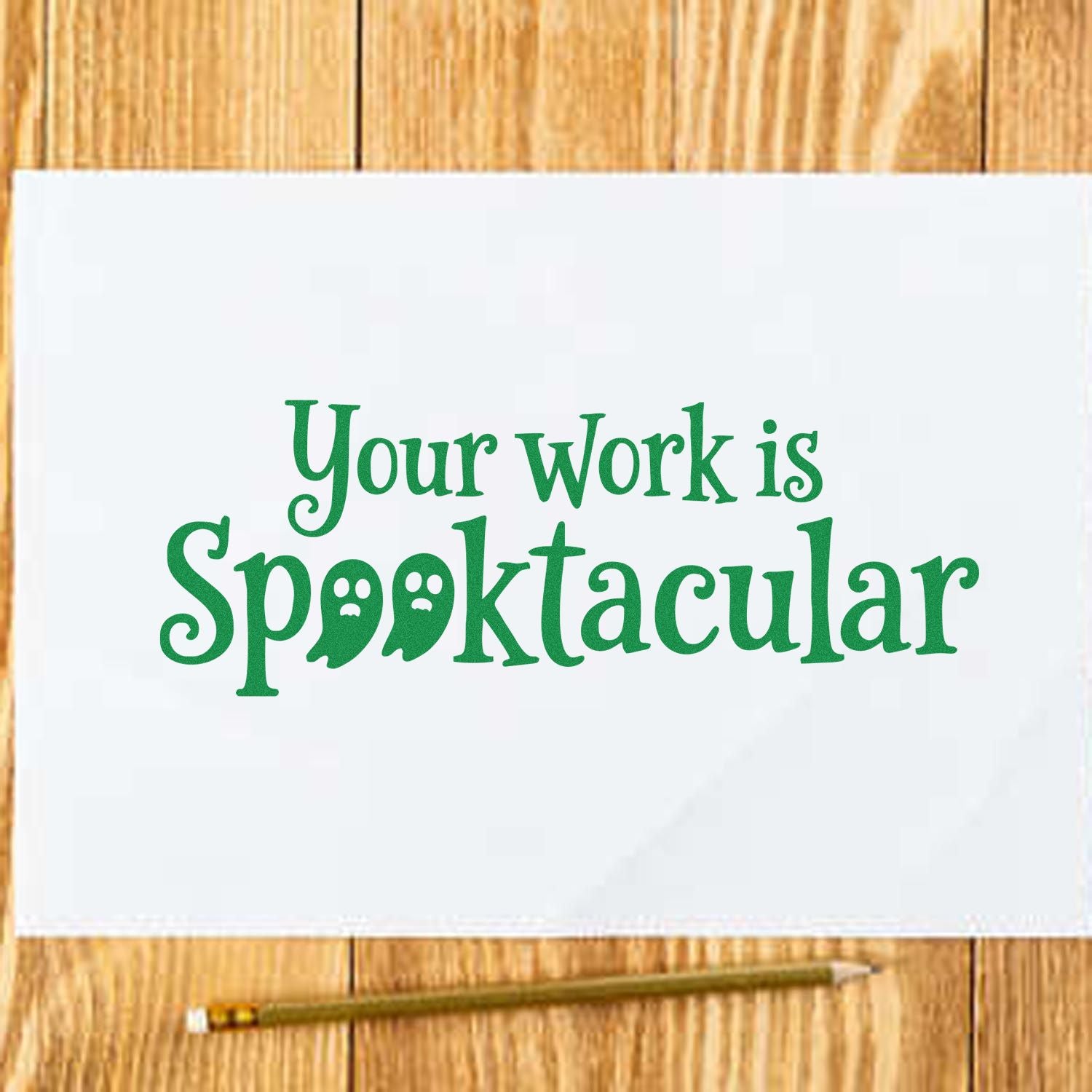 Green Halloween stamp and seal reading Your work is Spooktacular on white paper over wood, with pencil.
