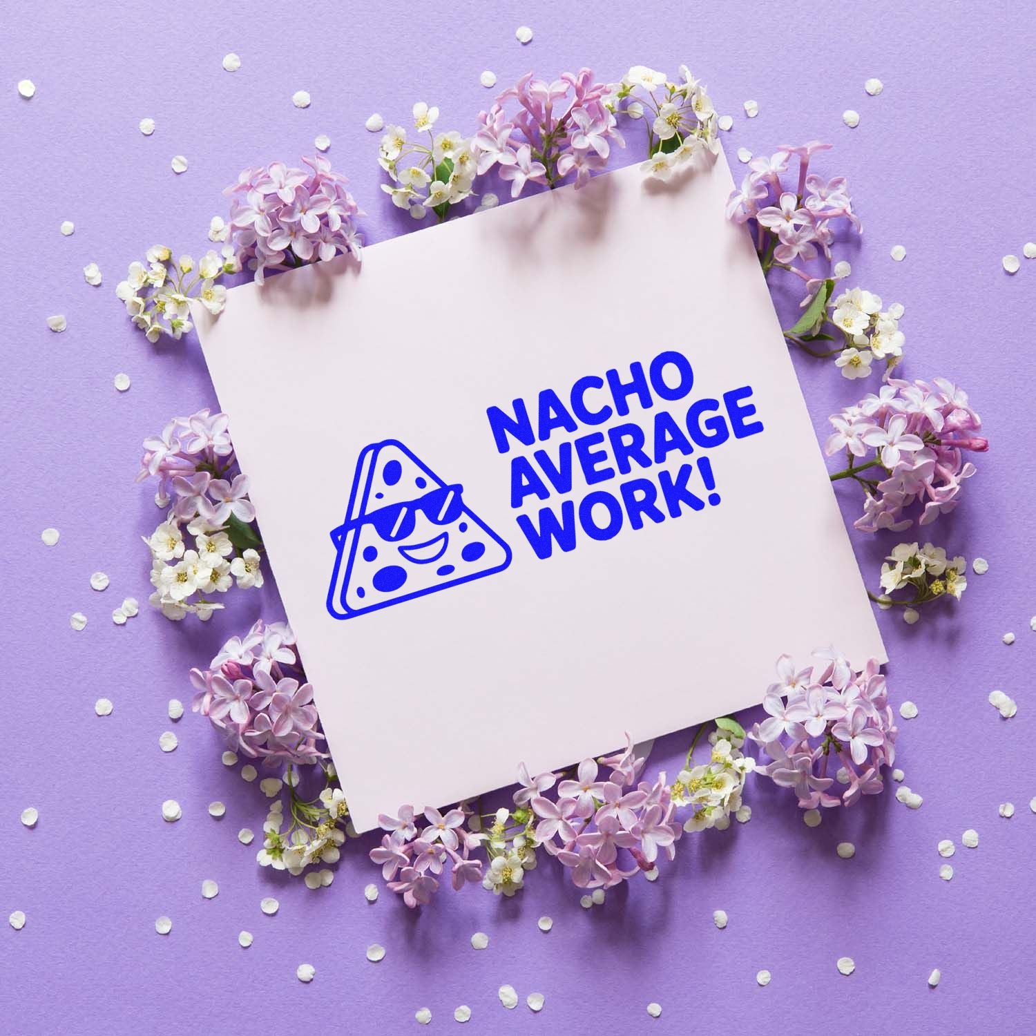 Blue cheese-shaped stamp/seal design reading NACHO AVERAGE WORK! on white card with lilac flowers and purple background.