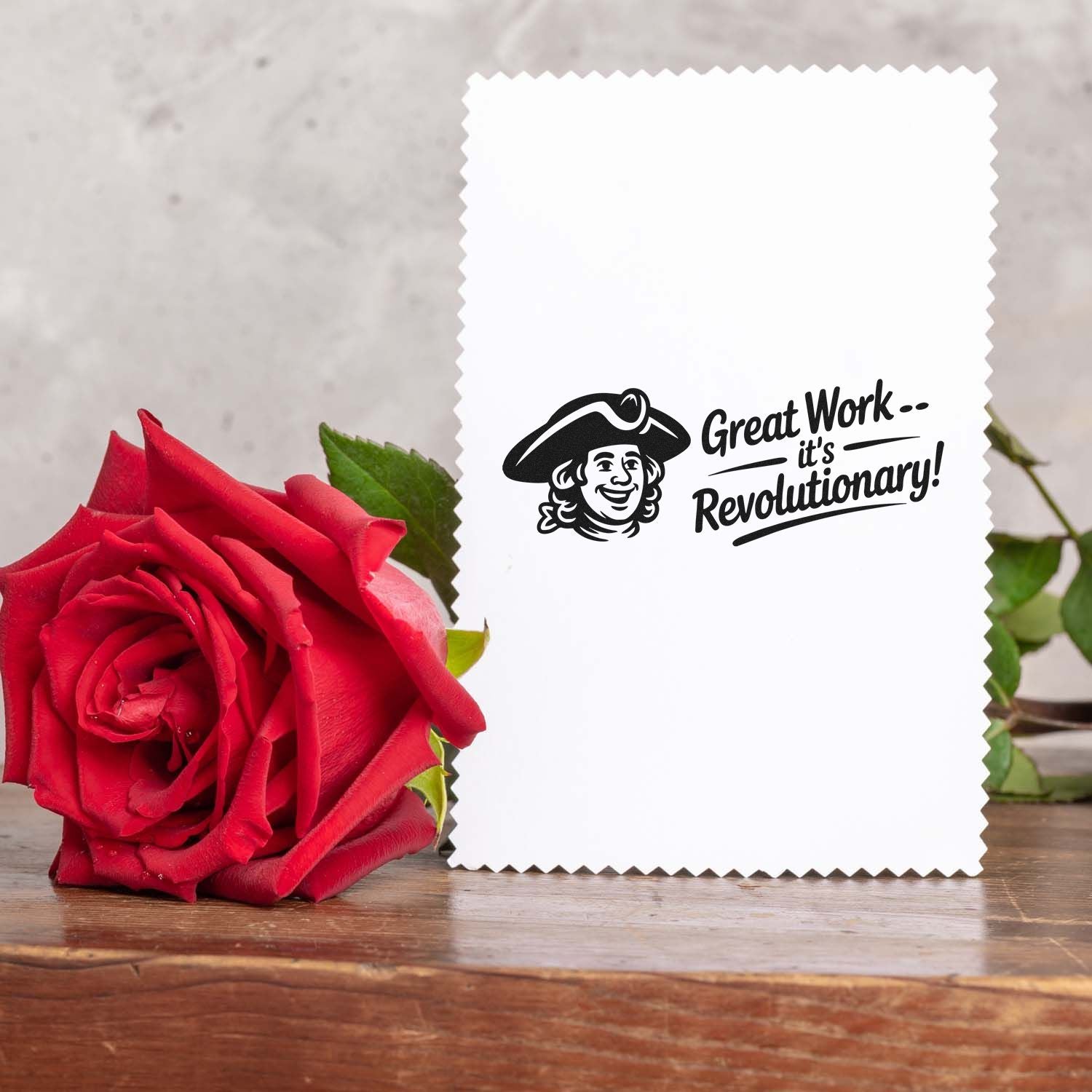 White scalloped-edge stamp and seal card with black Great Workits Revolutionary! design beside a red rose.