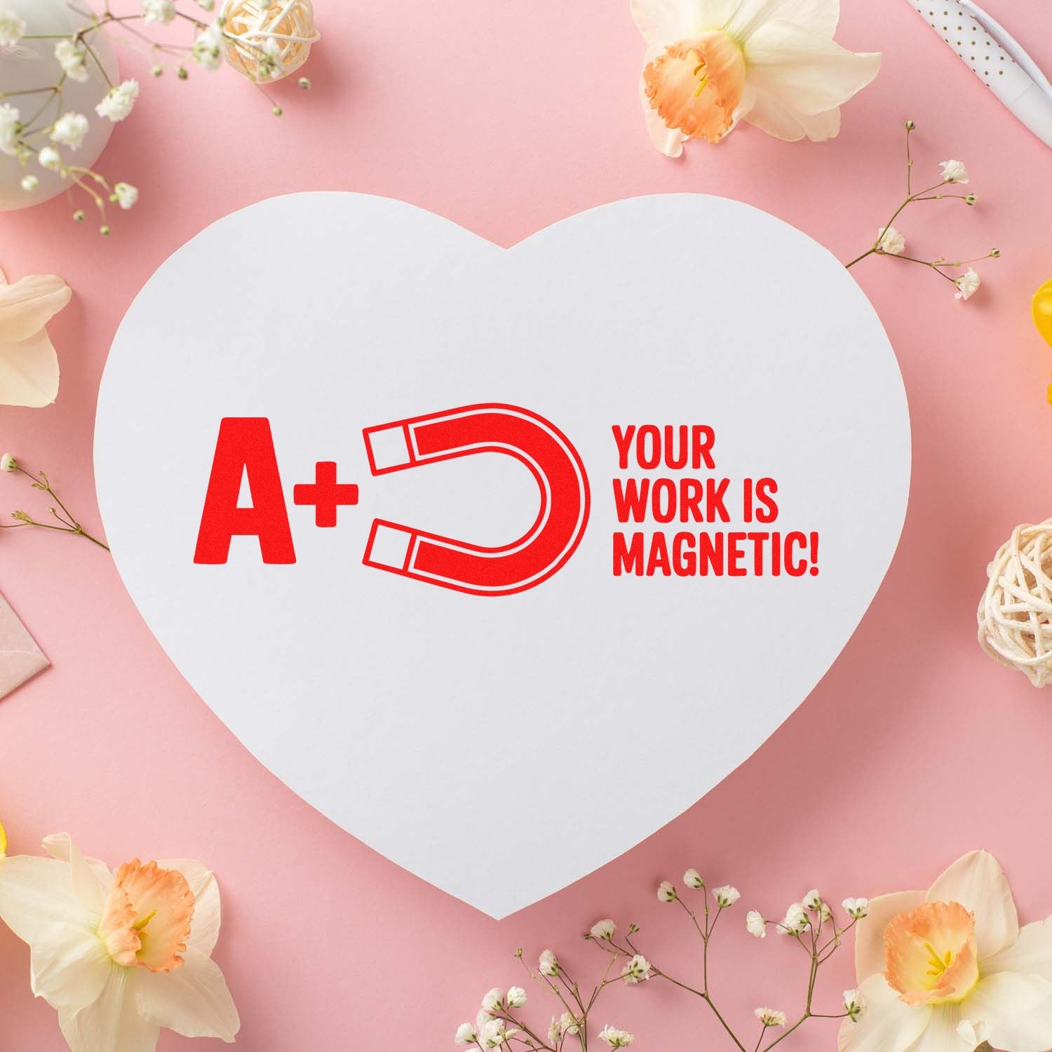 Heart-shaped white stamp and seal card with red A+ magnet logo and Your Work Is Magnetic! on pink floral background.