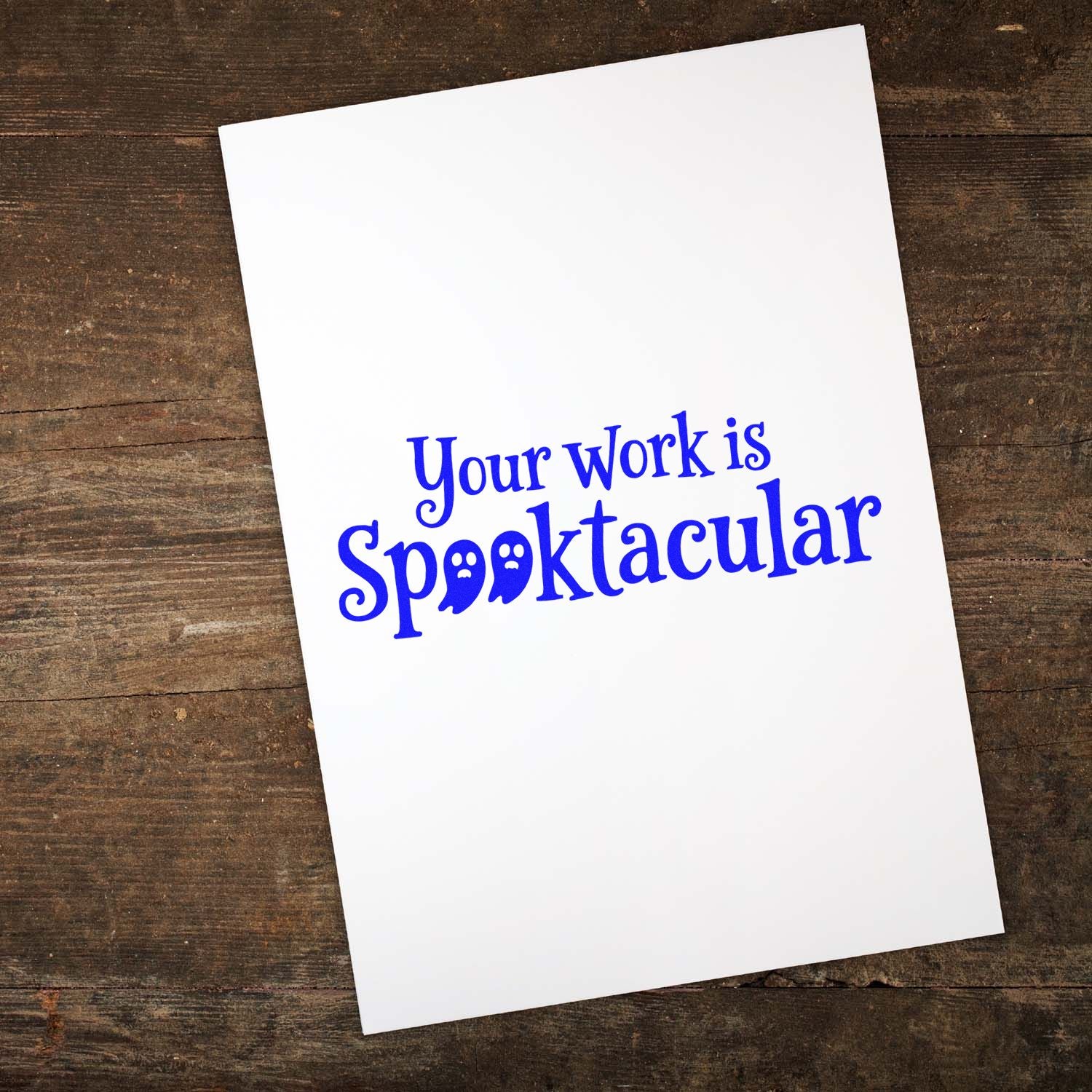 White card on rustic wood with a blue decorative stamp reading Your work is Spooktacular and ghost-shaped letters.