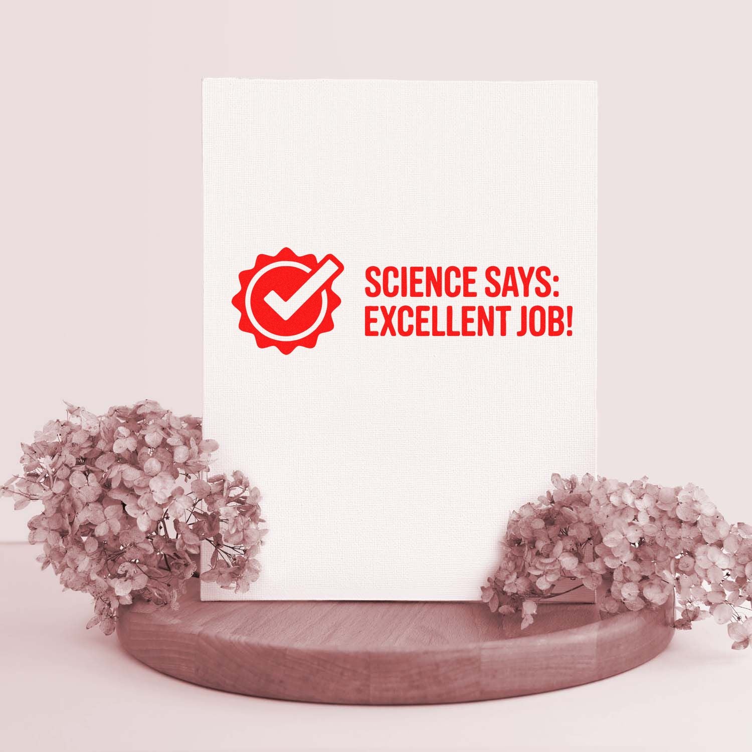 White stamp card with red seal and checkmark reading Science says: Excellent job!, displayed on wood stand with pink flowers.