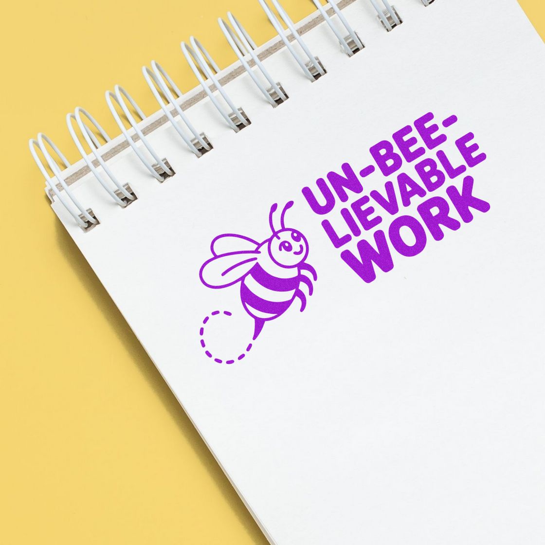 Purple stamp seal on white spiral notebook with bee icon and UN-BEE-LIEVABLE WORK text on yellow background.