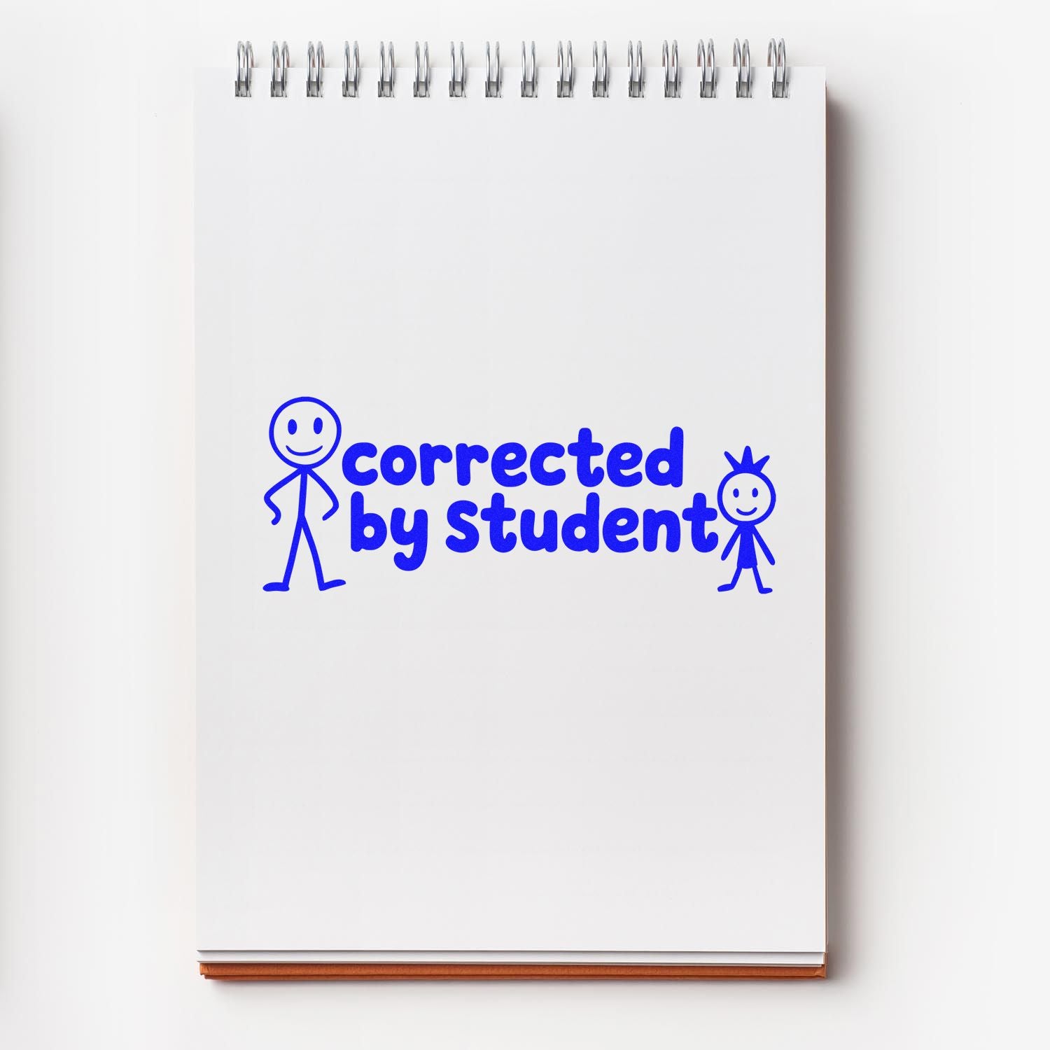 White spiral notebook stamped in blue with corrected by student and two stick figures, a rubber stamp and seal design.