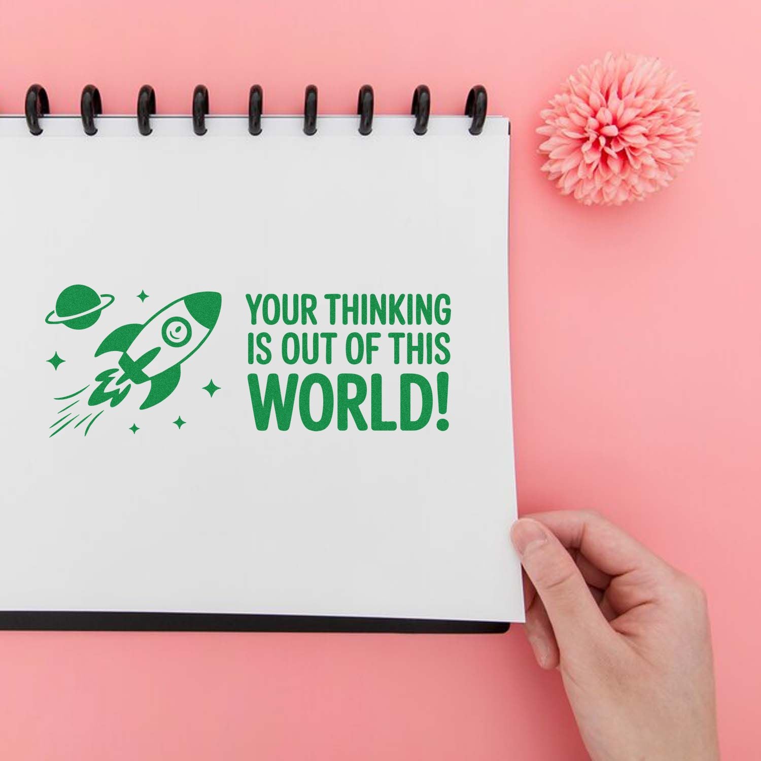 Green rubber stamp with rocket and planets on a white notebook, reading Your thinking is out of this world! on pink background.