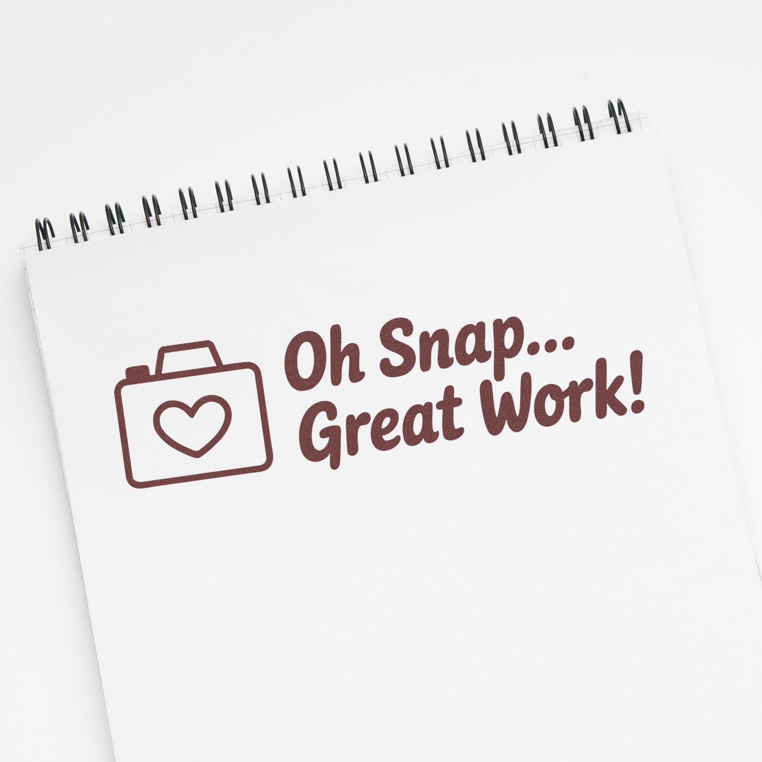 Maroon stamp seal reading Oh Snap... Great Work! with heart briefcase icon on a white spiral notepad.