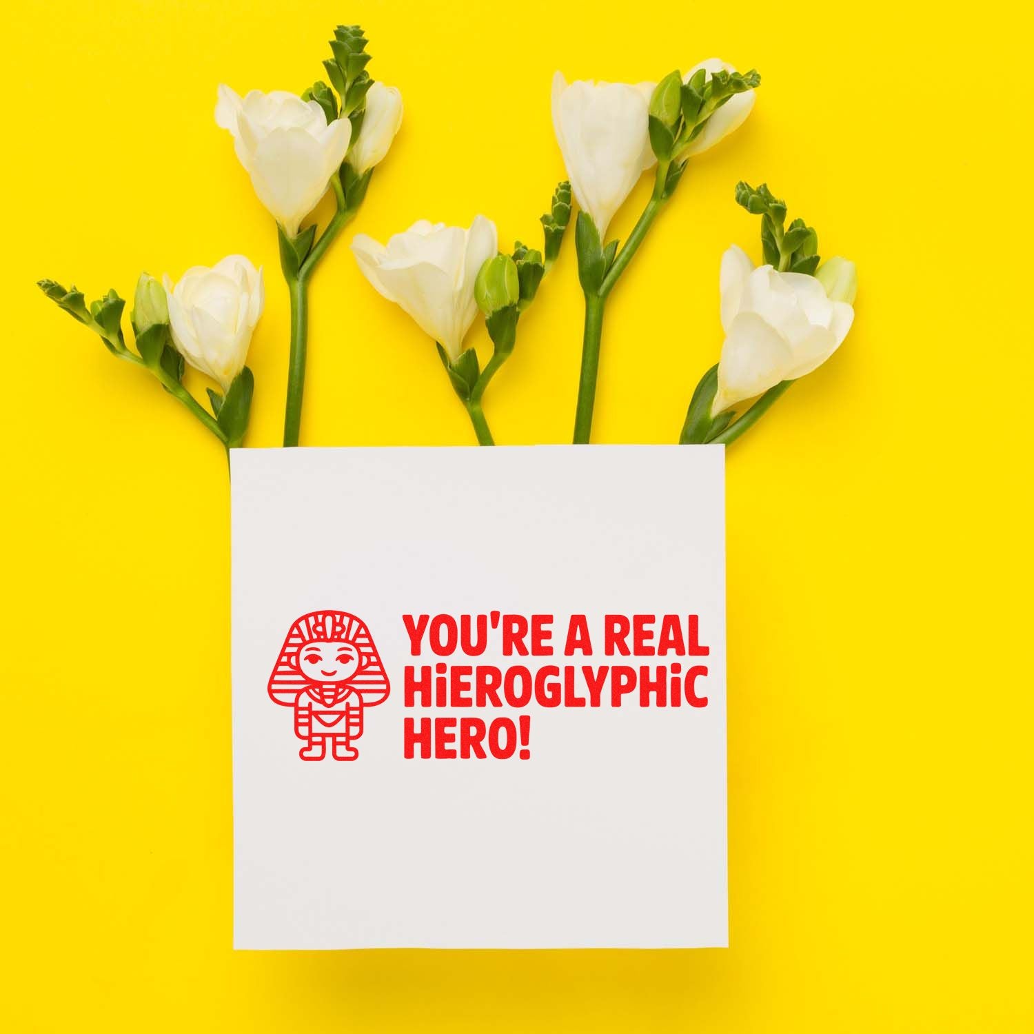 White stamp-and-seal card with red Egyptian-style hero stamp and text, framed by white flowers on a bright yellow background.