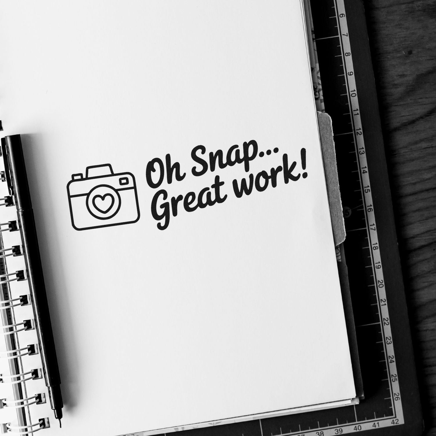 Black stamp/seal with camera icon and Oh Snap... Great work! on a white notebook page.