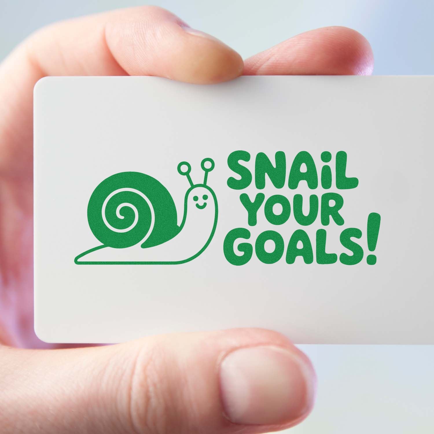 Green snail stamp seal with SNAIL YOUR GOALS! on a white card held in hand.