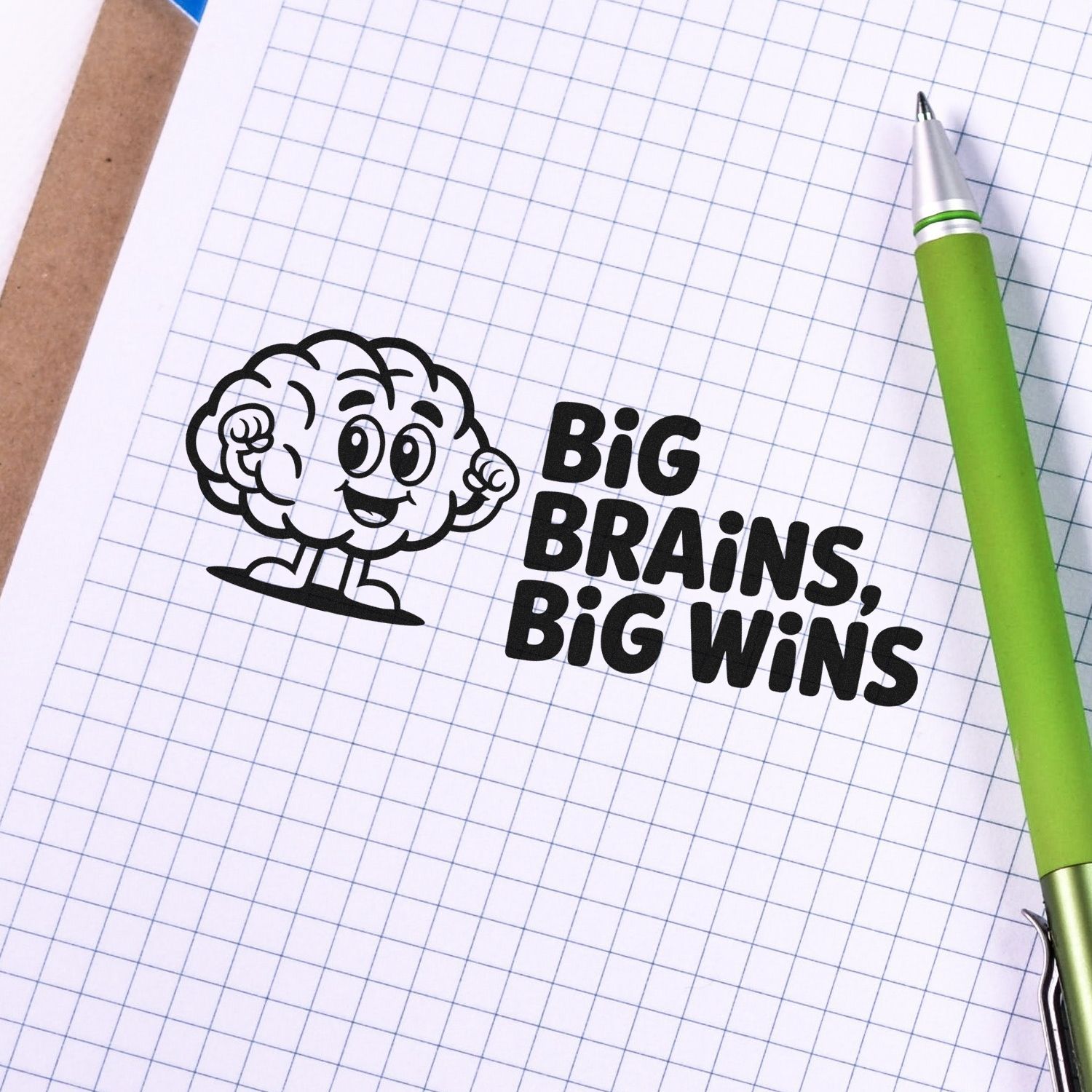 Black stamp seal with cartoon brain and BIG BRAINS, BIG WINS on graph paper beside a green pen.