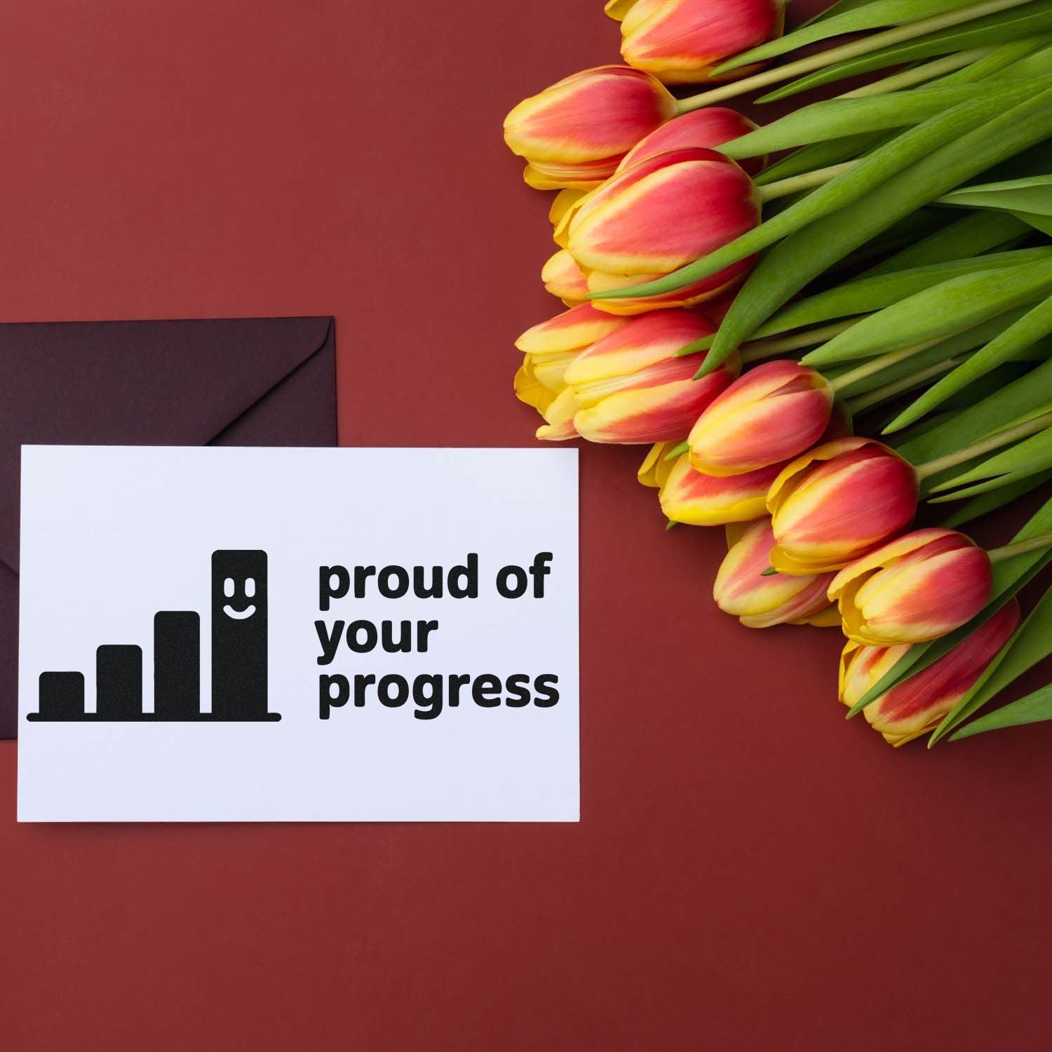 White stamp card with black proud of your progress seal, beside pink-yellow tulips on a burgundy background.