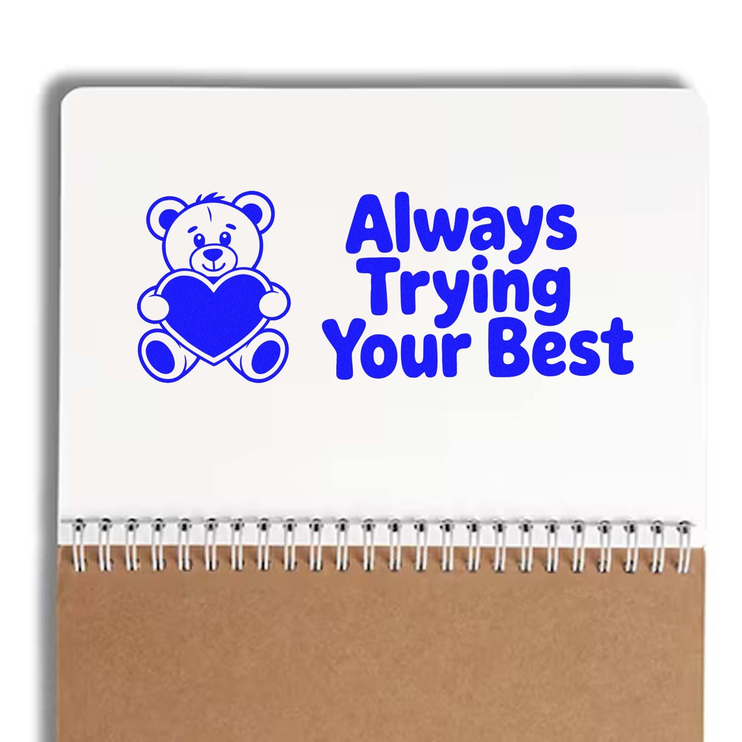 Blue teddy bear stamp and seal design with heart and Always Trying Your Best on a white spiral notebook.
