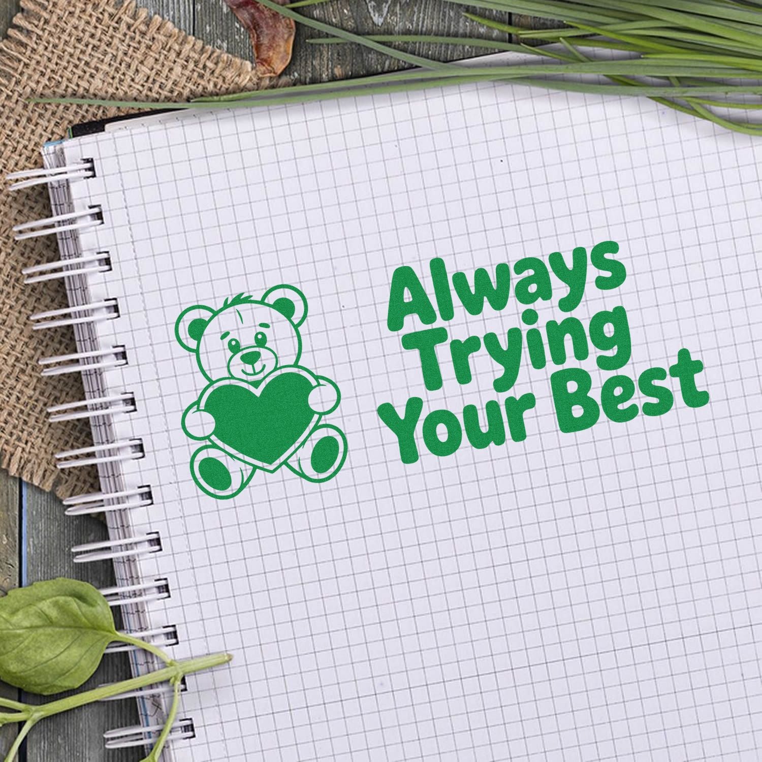 Green stamp and seal design with a teddy bear holding a heart and bold Always Trying Your Best text on graph paper.