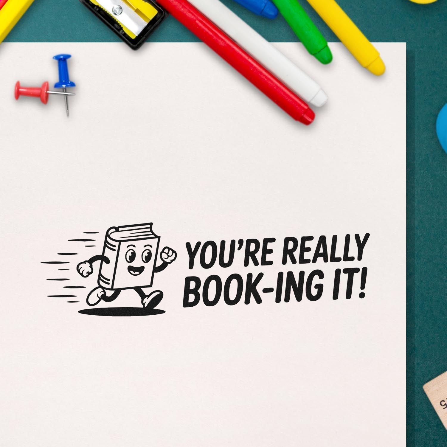 Black stamp seal on white paper shows a running book mascot and YOURE REALLY BOOK-ING IT! with colorful pens and pushpins.