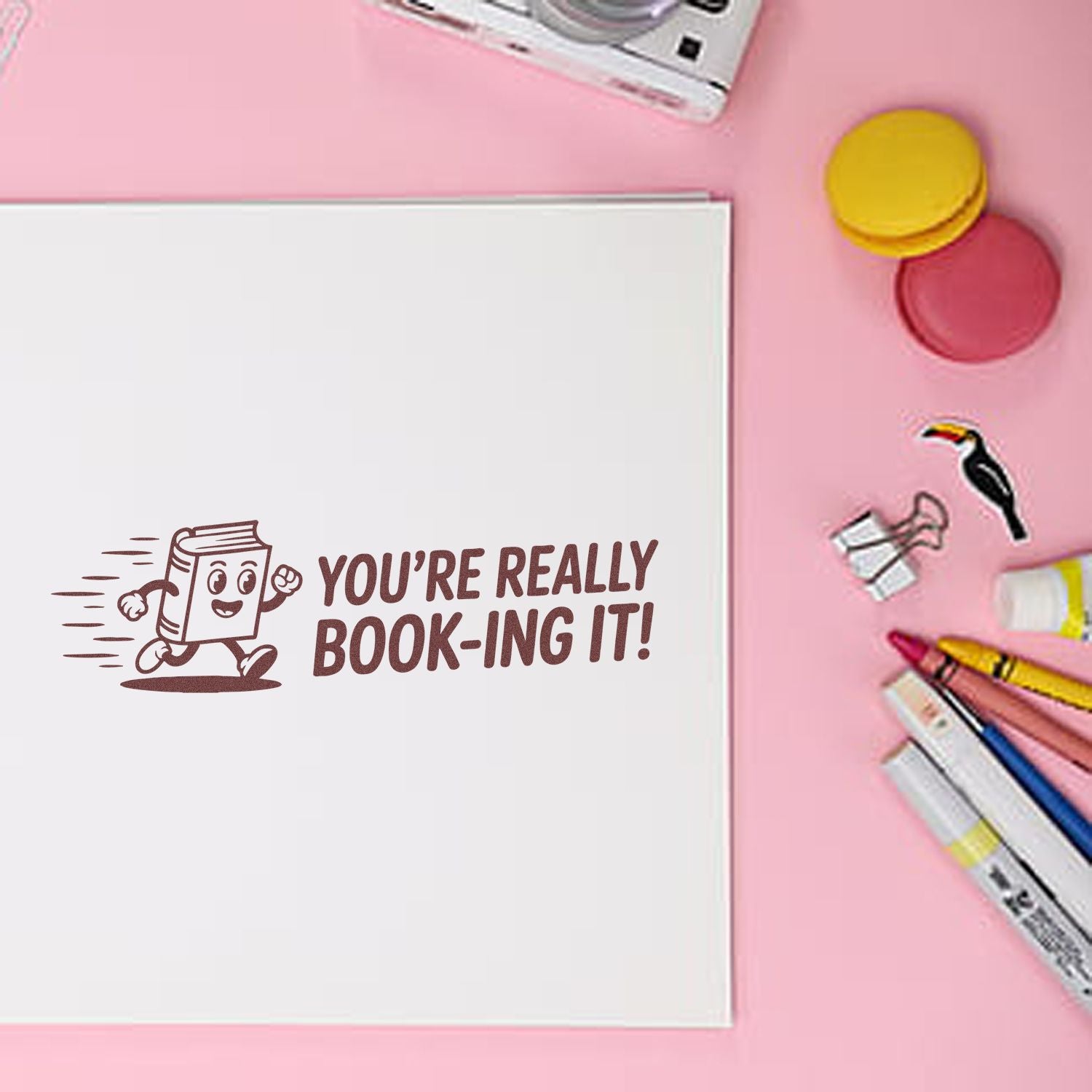 Brown book-themed stamp on white paper with pink background, colorful markers, and yellow and pink seal pads.