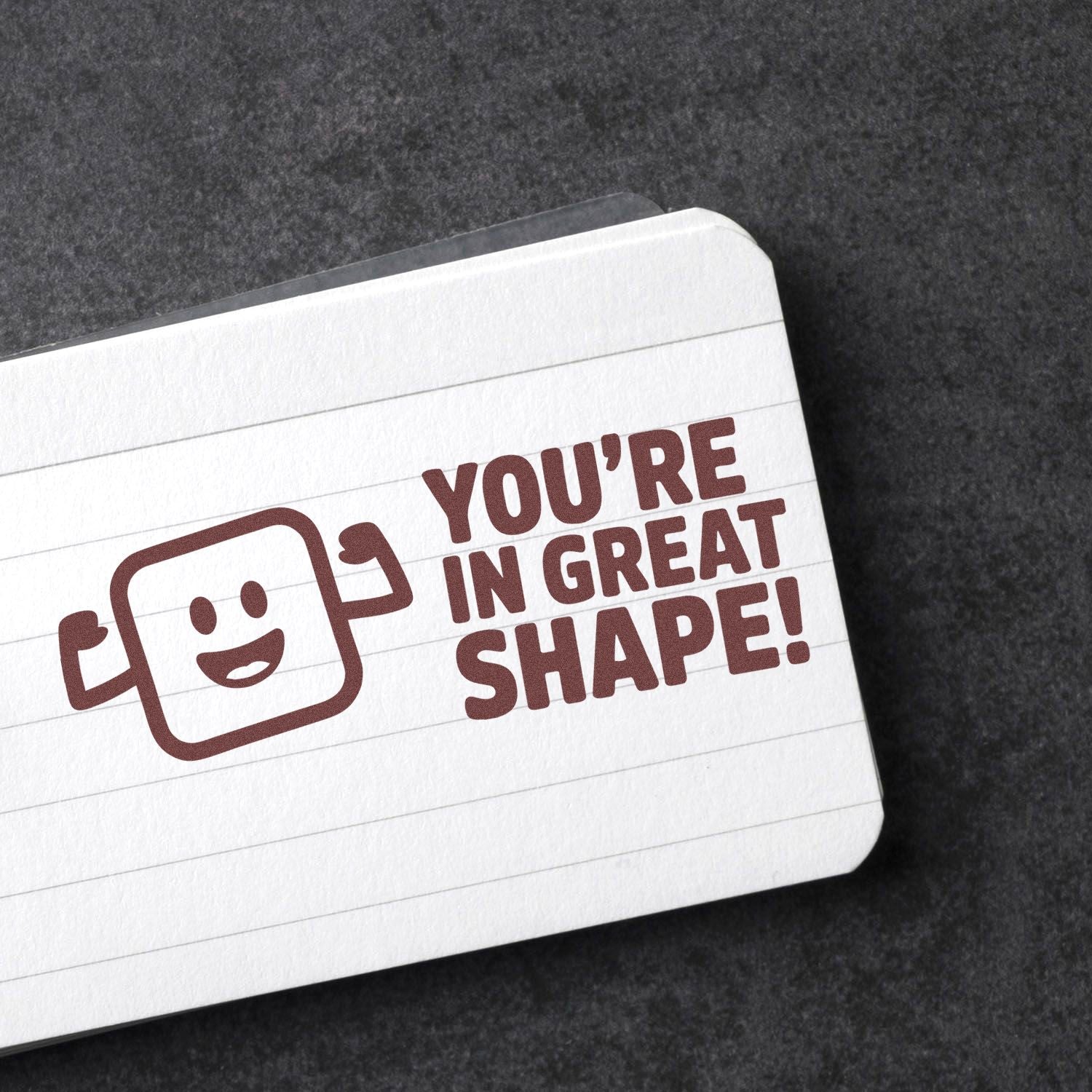 Maroon self-inking stamp and seal with smiling flexing icon and Youre in great shape! on a white lined card.