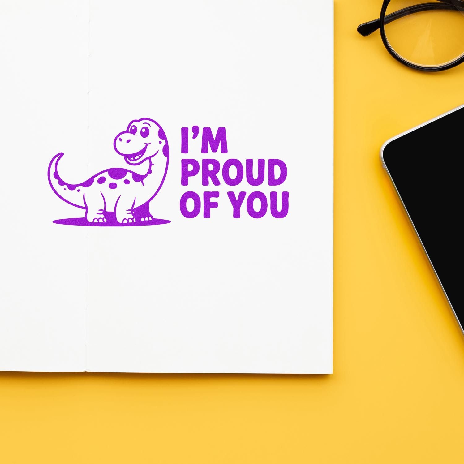 Purple dinosaur stamp with Im proud of you seal on white paper, set on a yellow desk with glasses and phone.