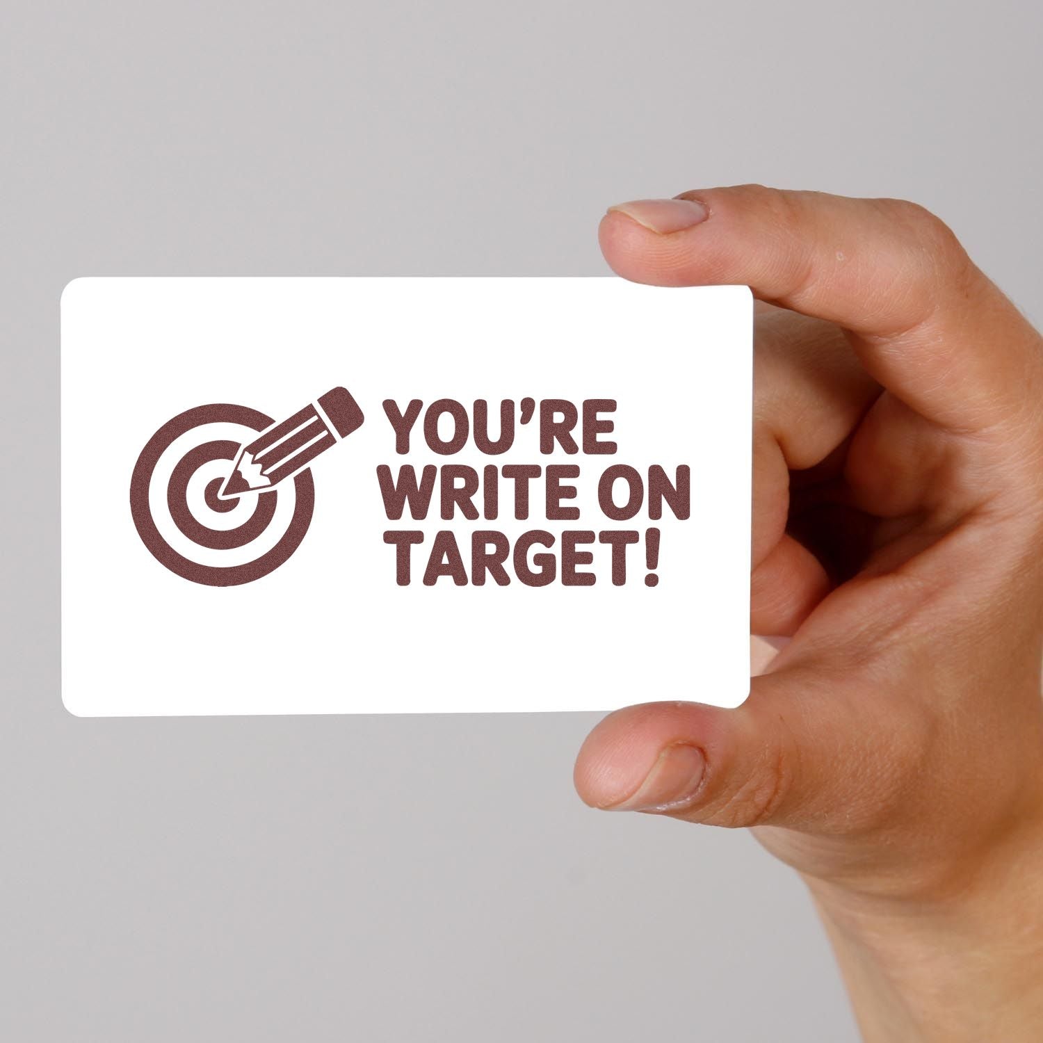 Hand holding a white custom stamp and seal card with brown target-and-pencil logo and Youre write on target! text.