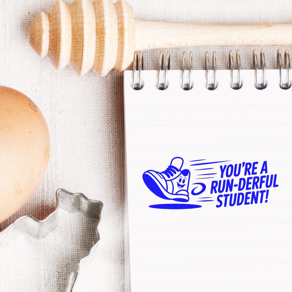 Blue stamp and seal reading Youre a run-derful student! on a white spiral notebook, with a smiling sneaker and wooden handle.