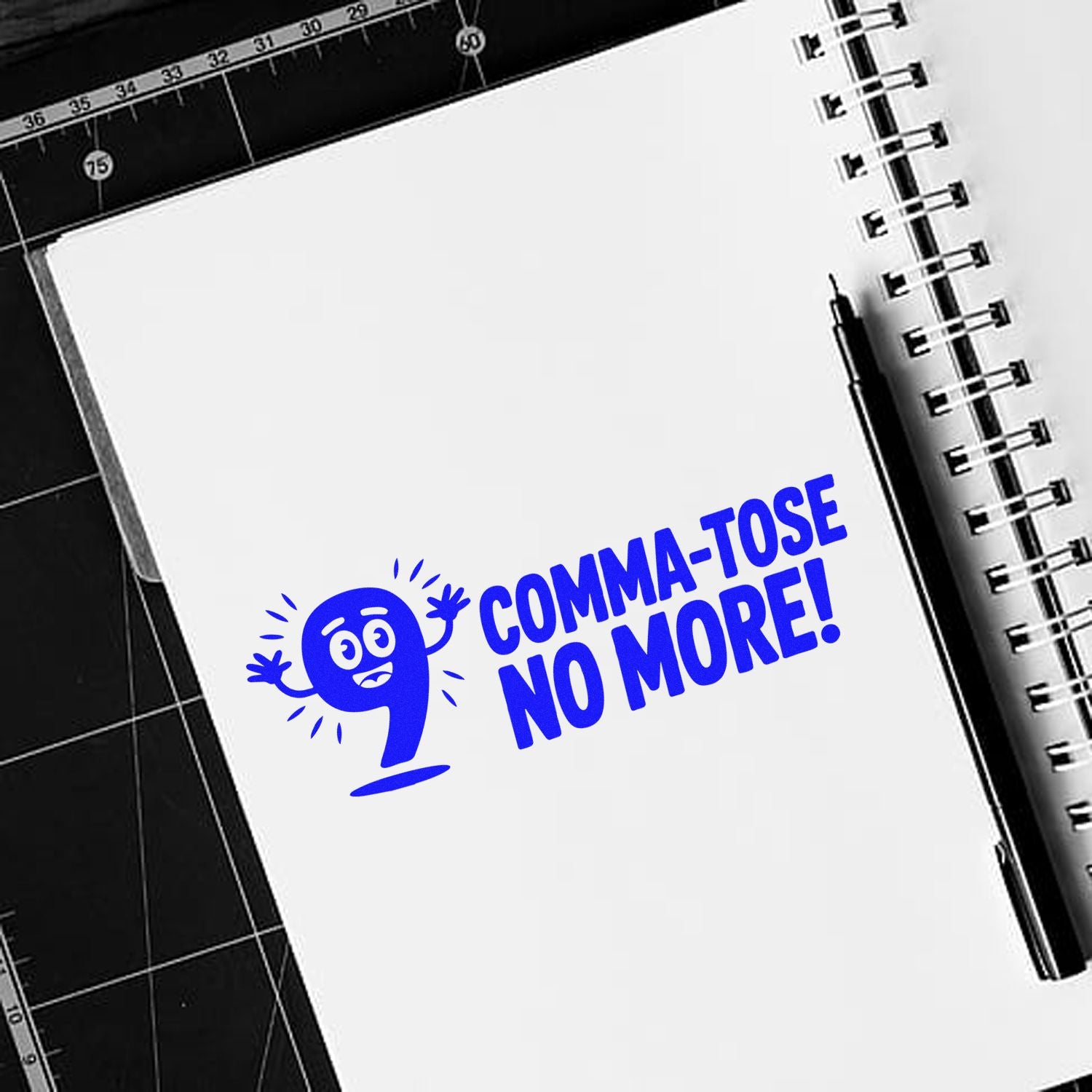 Blue custom stamp and seal reading COMMA-TOSE NO MORE! on a white notebook page beside a black pen and spiral binding.