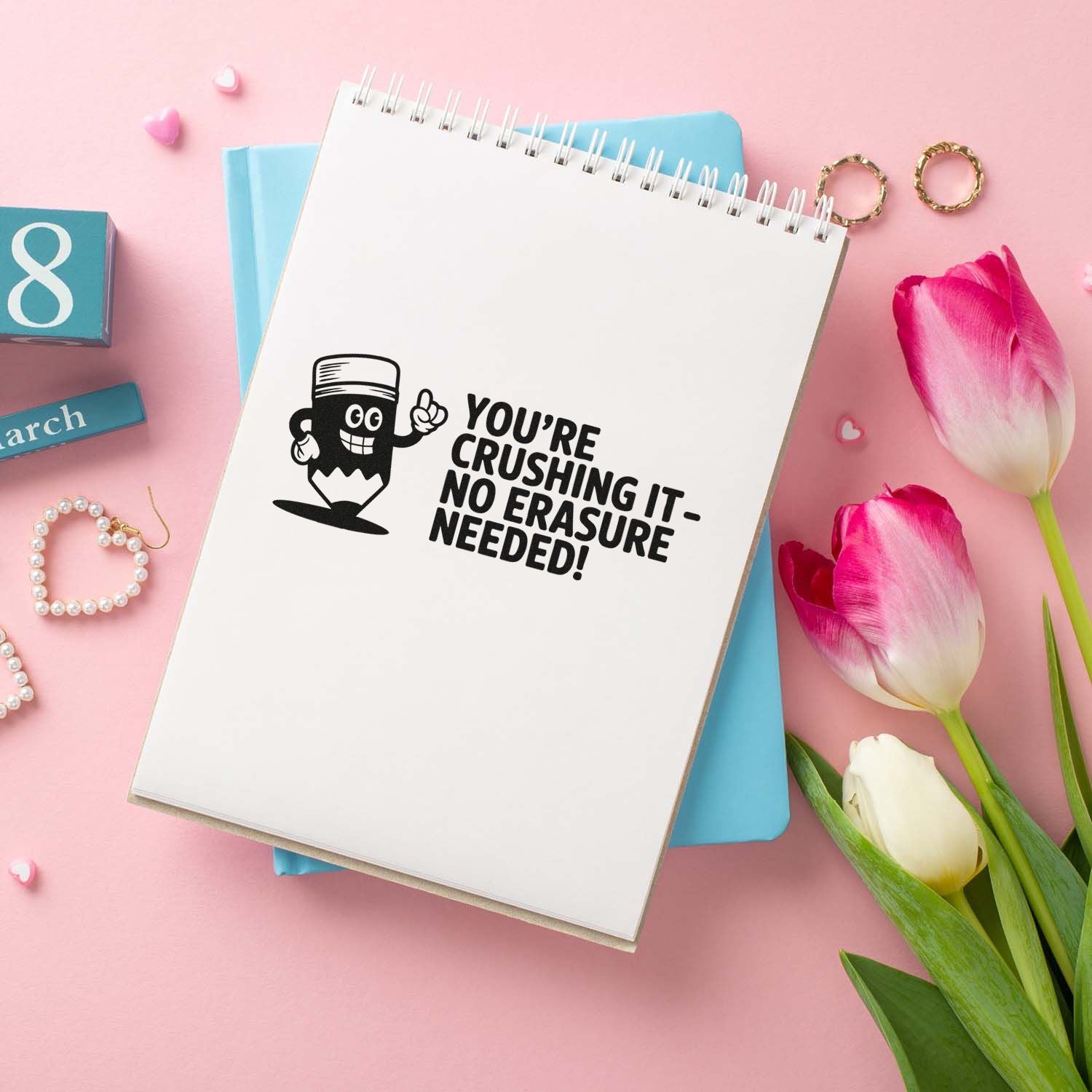 Black motivational stamp/seal on white spiral notebook, with pink tulips and blue stationery on a blush background.