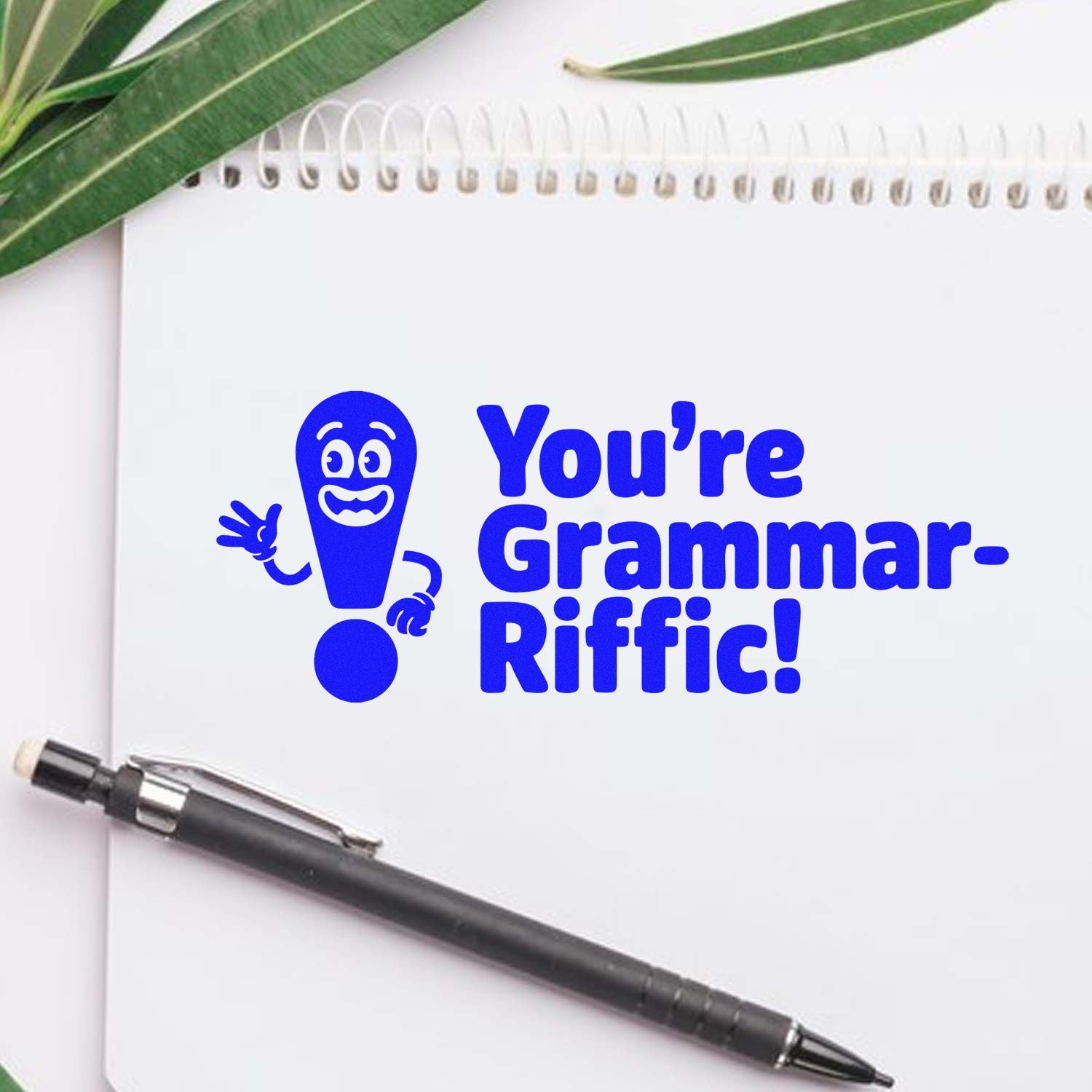 Blue grammar-riffic rubber stamp seal on white notebook, with smiling exclamation mark and pen