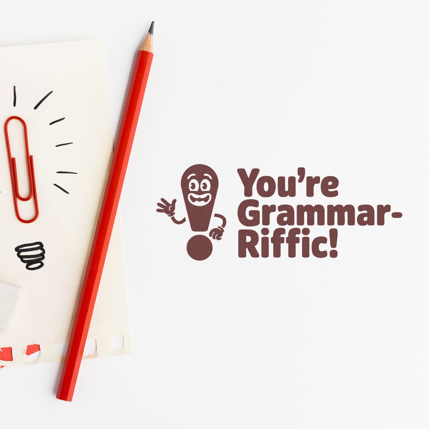 Brown grammar stamp seal reading Youre Grammar-Riffic! beside a red pencil, red paperclip, and notebook paper mockup.