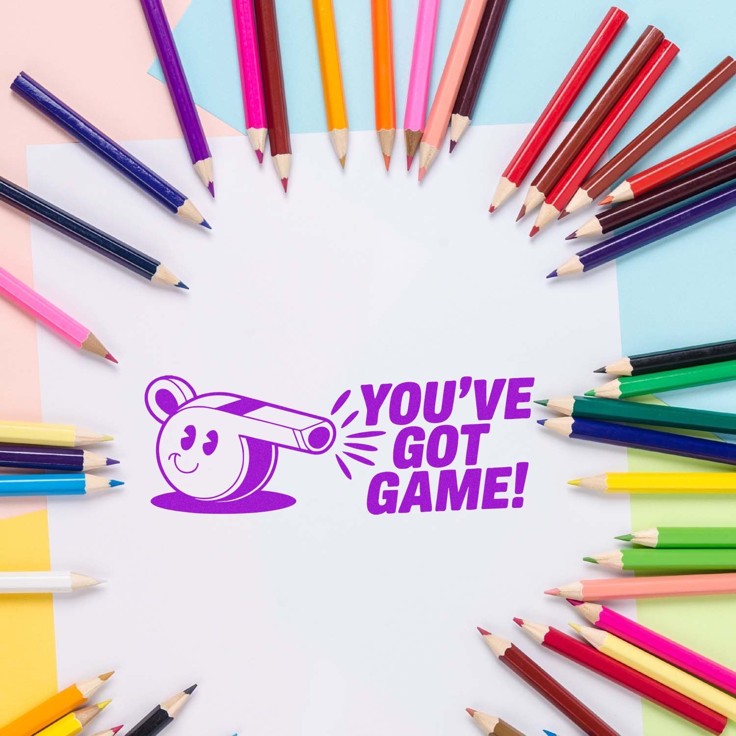 Purple rubber stamp seal with Youve Got Game! on white paper, framed by colorful pencils on pastel pink, blue, and yellow backgrounds.