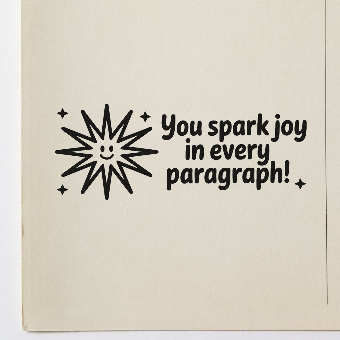 Black stamp seal on cream paper with smiling starburst and text, You spark joy in every paragraph!