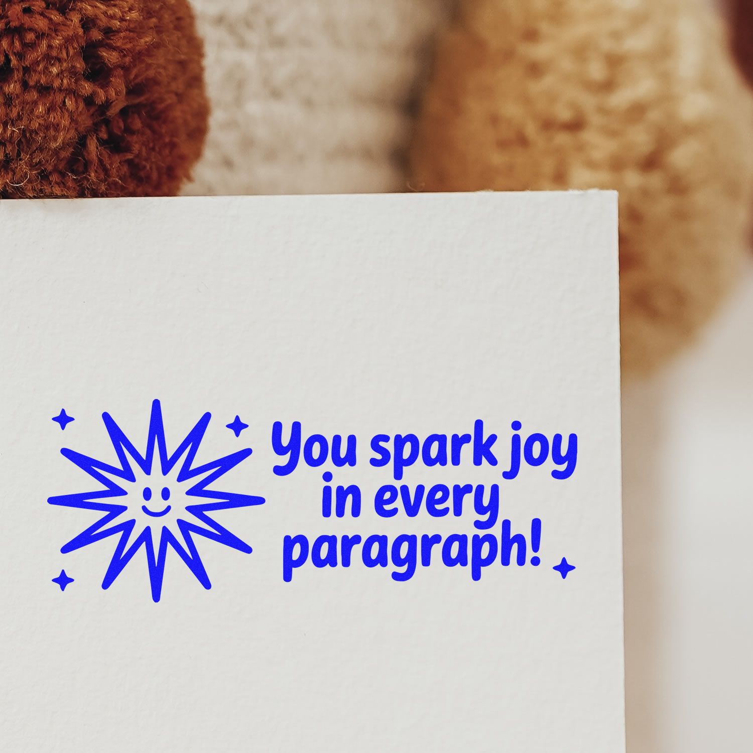 Blue stamp seal with smiling starburst and You spark joy in every paragraph! on white paper.