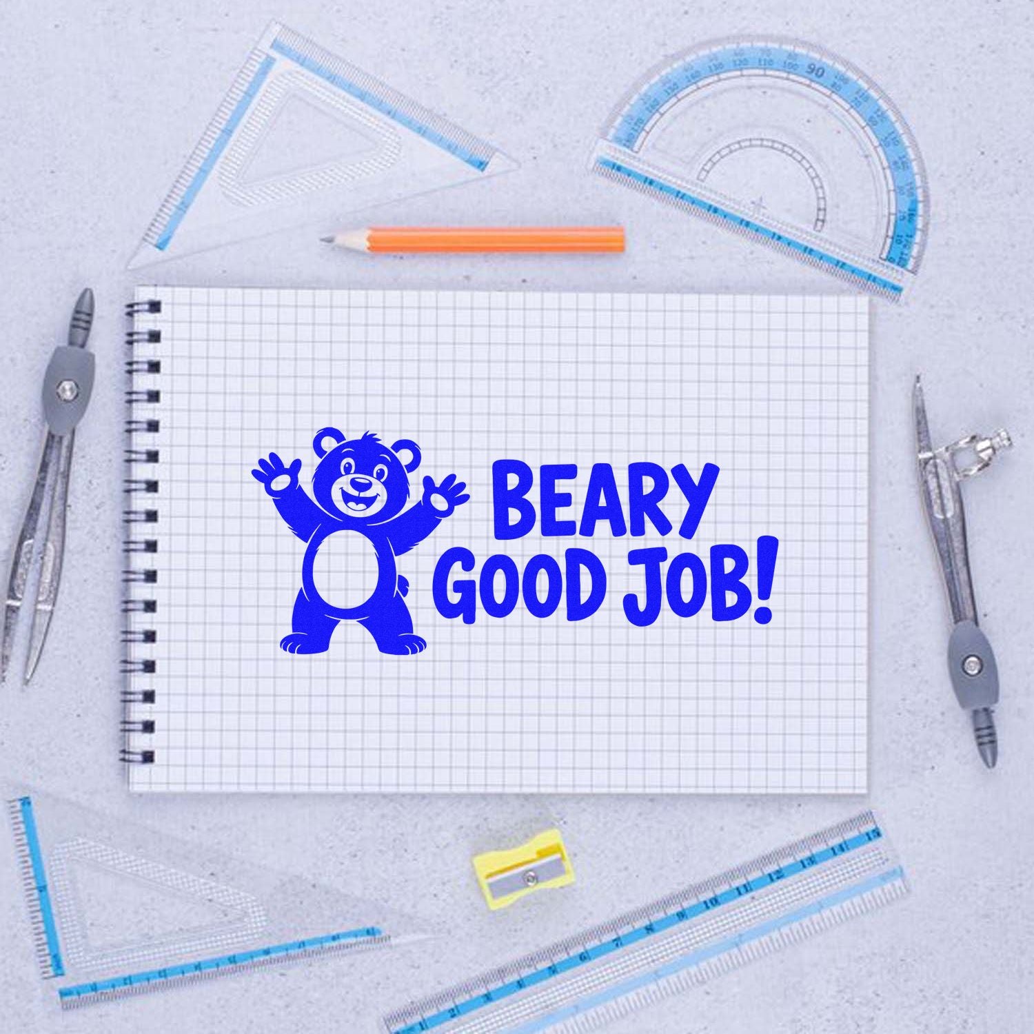 Blue Beary Good Job! stamp seal with smiling bear on graph paper, surrounded by rulers, pencil, and compass tools.