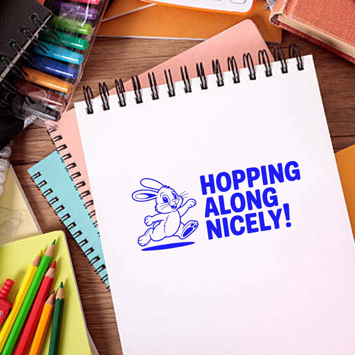 Blue bunny stamp and seal on white spiral notebook reads Hopping Along Nicely! with colorful stationery.