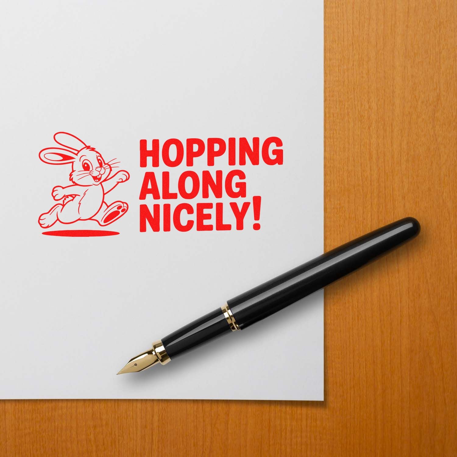 Red bunny rubber stamp and seal reading Hopping Along Nicely! beside a black fountain pen on white paper.