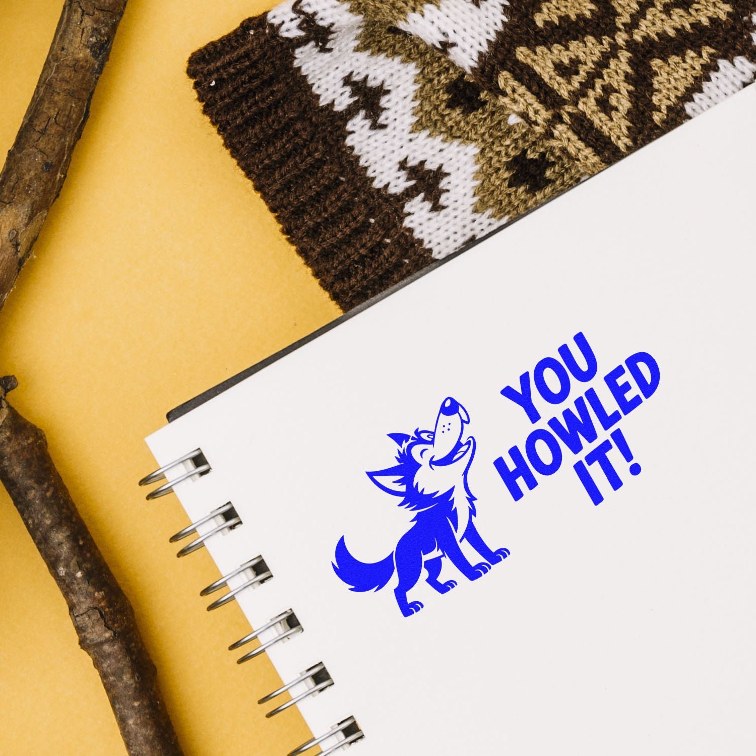 Blue wolf stamp seal with You Howled It! on a white spiral notebook, set on a yellow background with rustic wood accents.