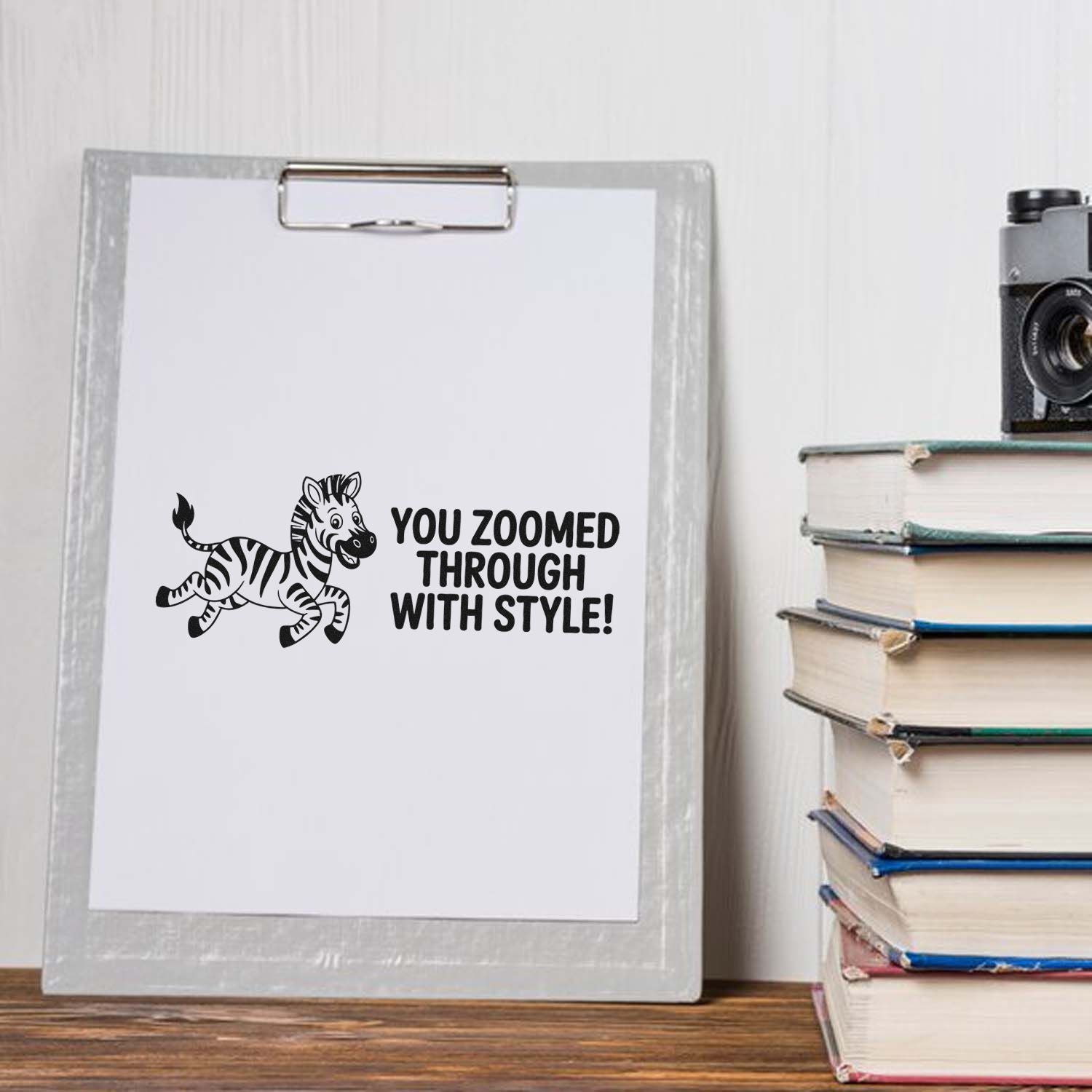 Custom black zebra stamp and seal on a clipboard with white paper, beside stacked books and a camera.