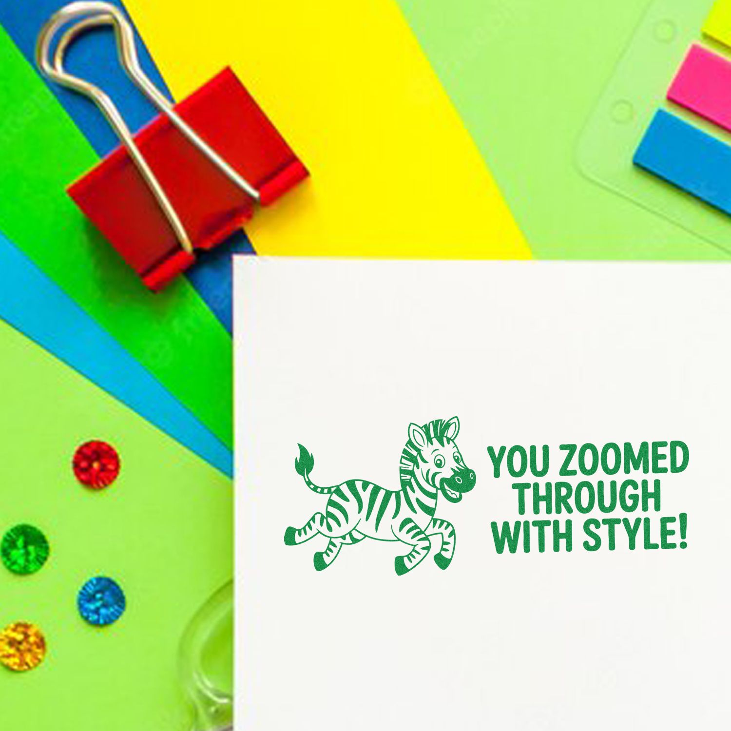 Green zebra stamp seal on white card with You Zoomed Through with Style! beside neon paper, binder clip, and sequins.