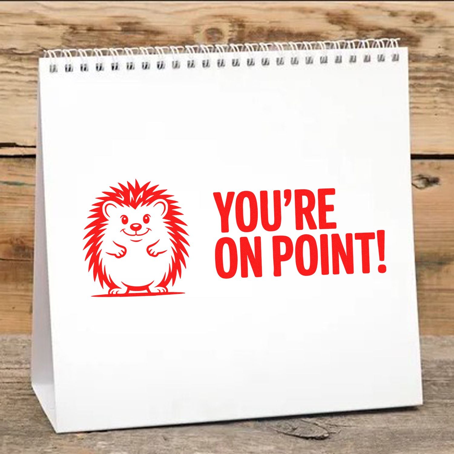 Red hedgehog stamp and seal design with YOURE ON POINT! in red on a white spiral pad over a wood background.