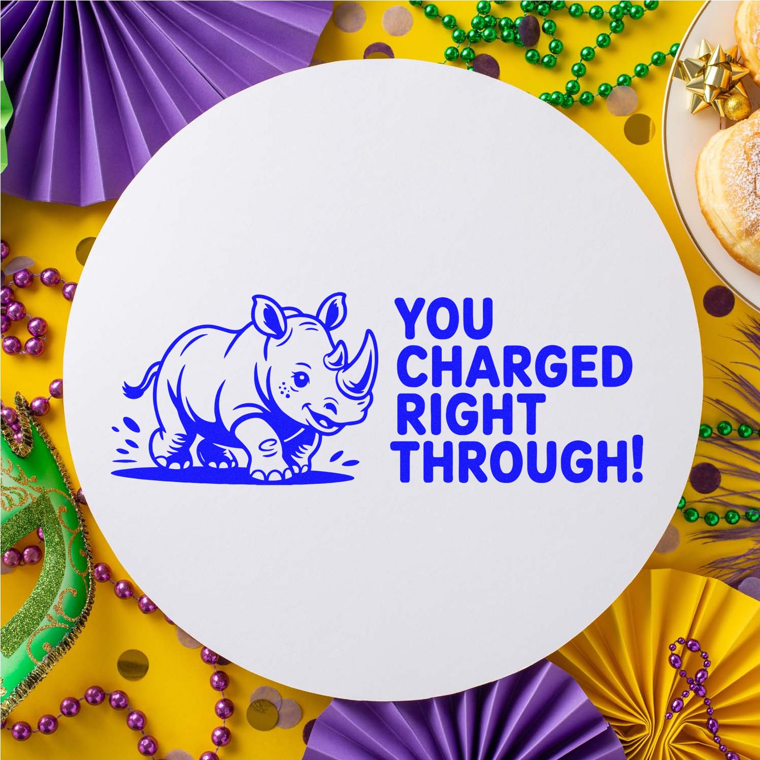 Blue rhinoceros stamp seal with You Charged Right Through! on a white round card amid purple, gold, and green Mardi Gras decor.