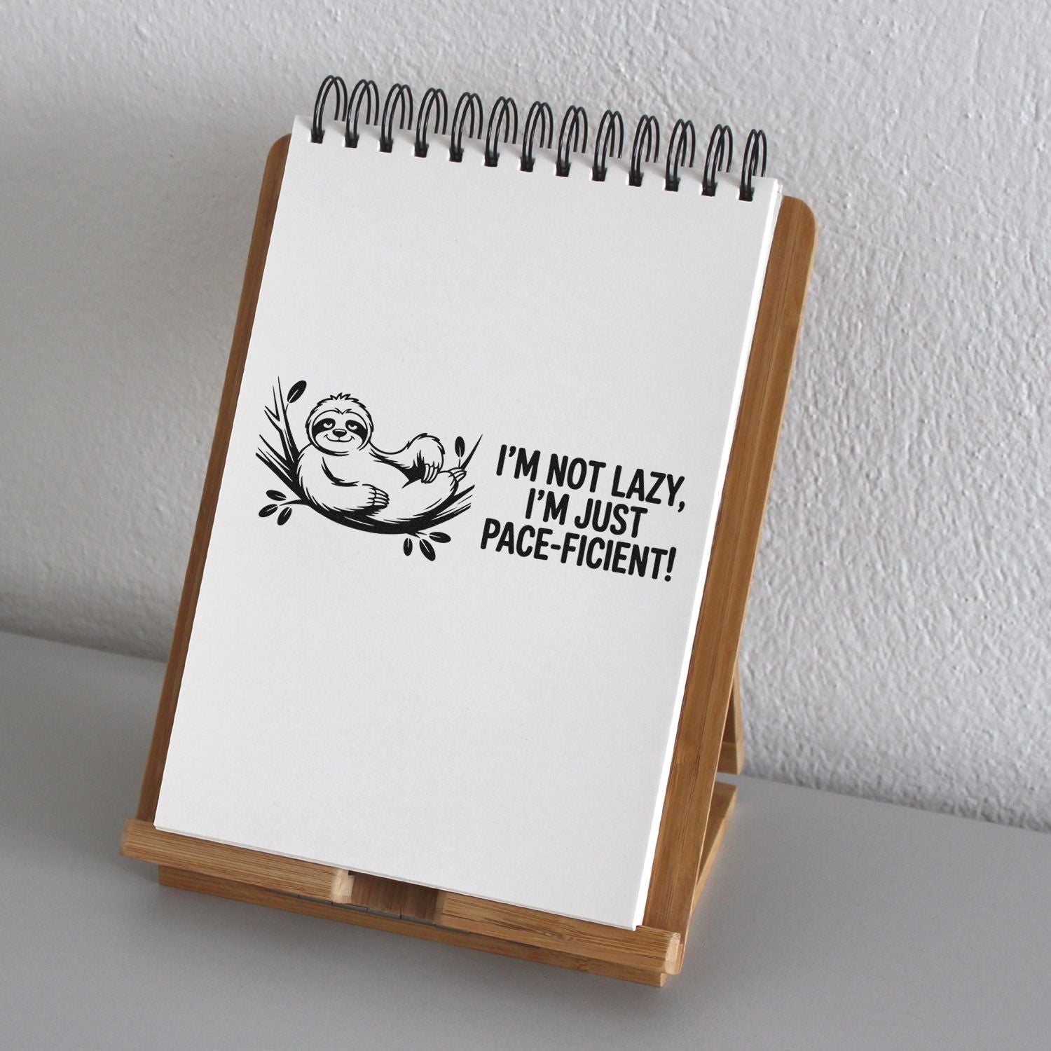 White spiral notepad on bamboo stand with black sloth custom stamp and Im not lazy, Im just pace-ficient! text.