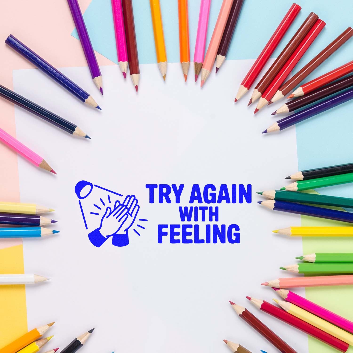Blue self-inking stamp and seal reading Try Again With Feeling, framed by colorful pencils on white paper.