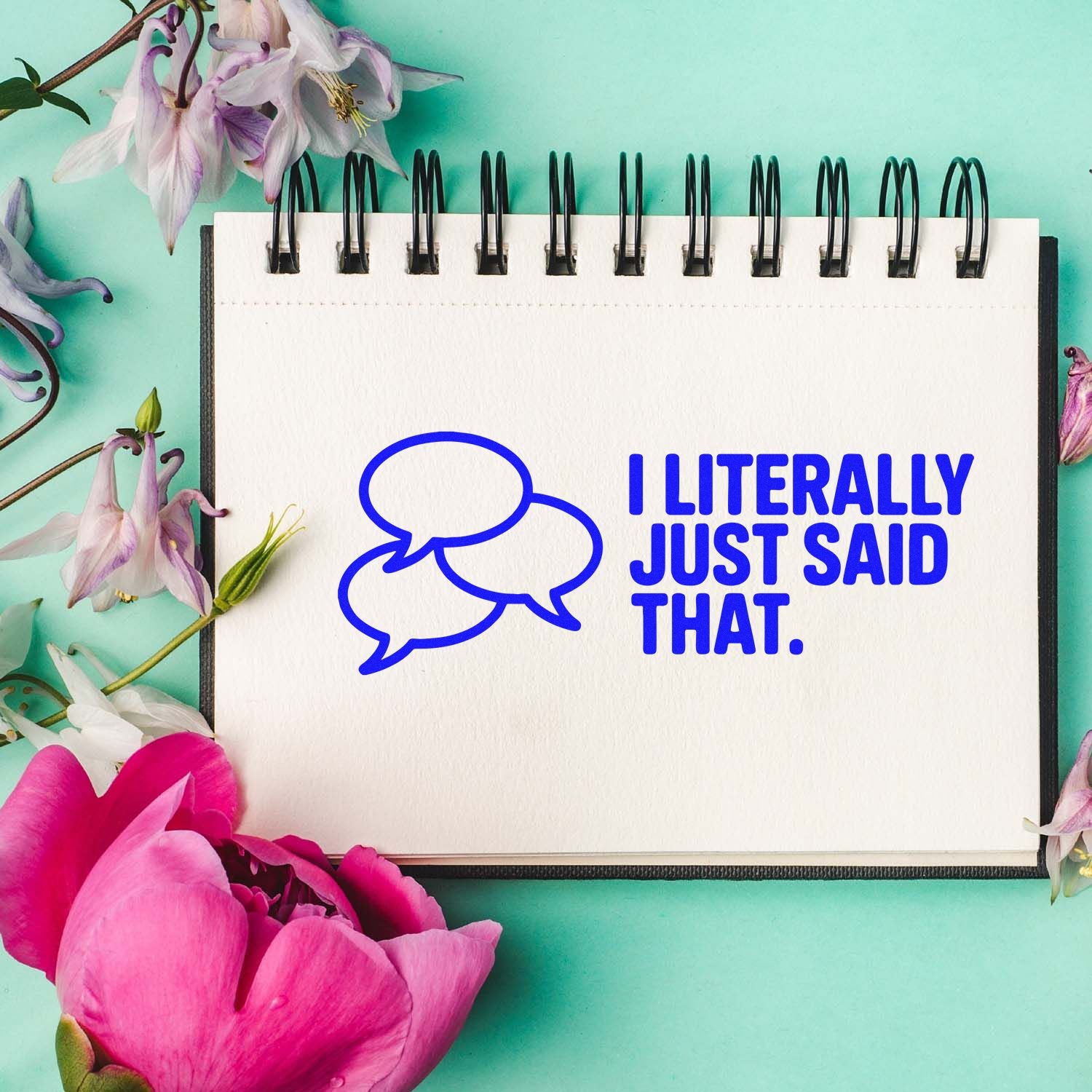 Blue speech-bubble stamp and seal reading I LITERALLY JUST SAID THAT. on a white notebook, with pink flowers on teal.