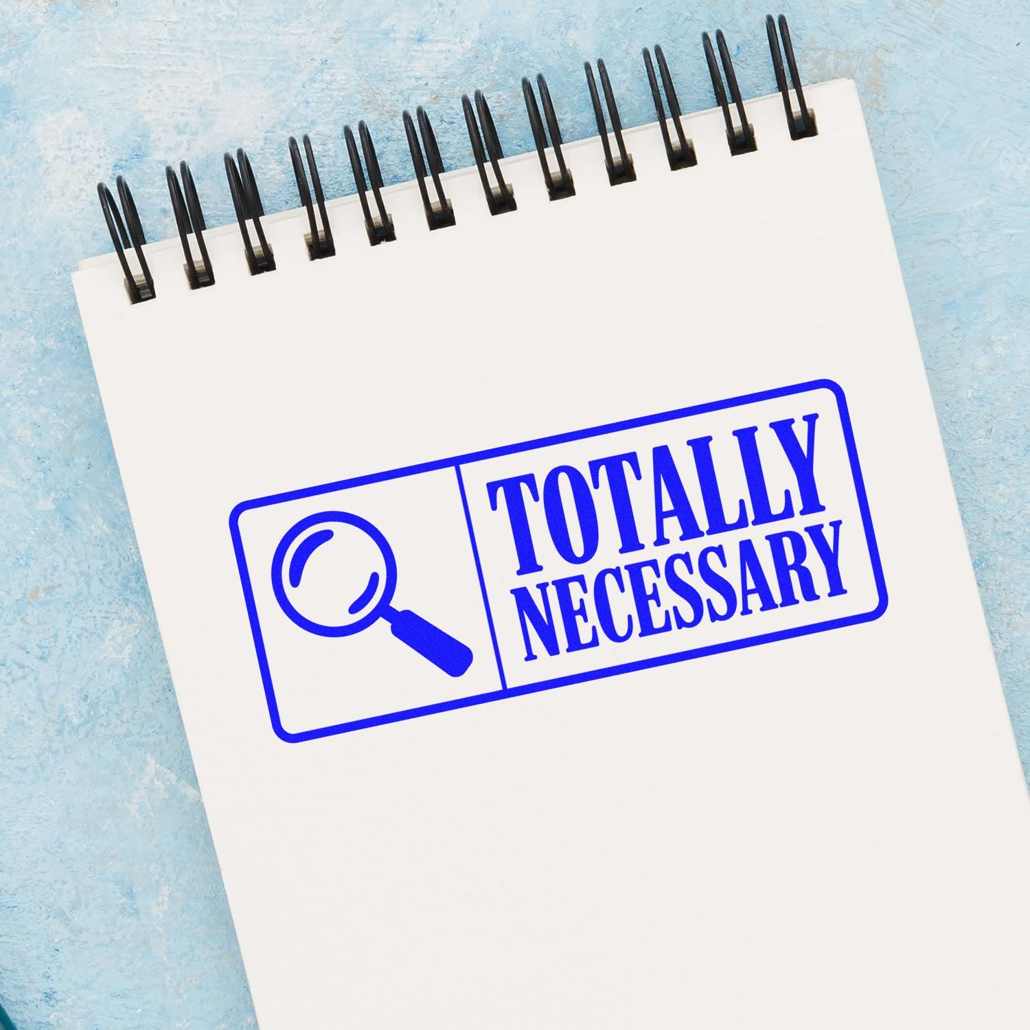 Blue Totally Necessary stamp seal with magnifying glass icon on a white spiral notebook