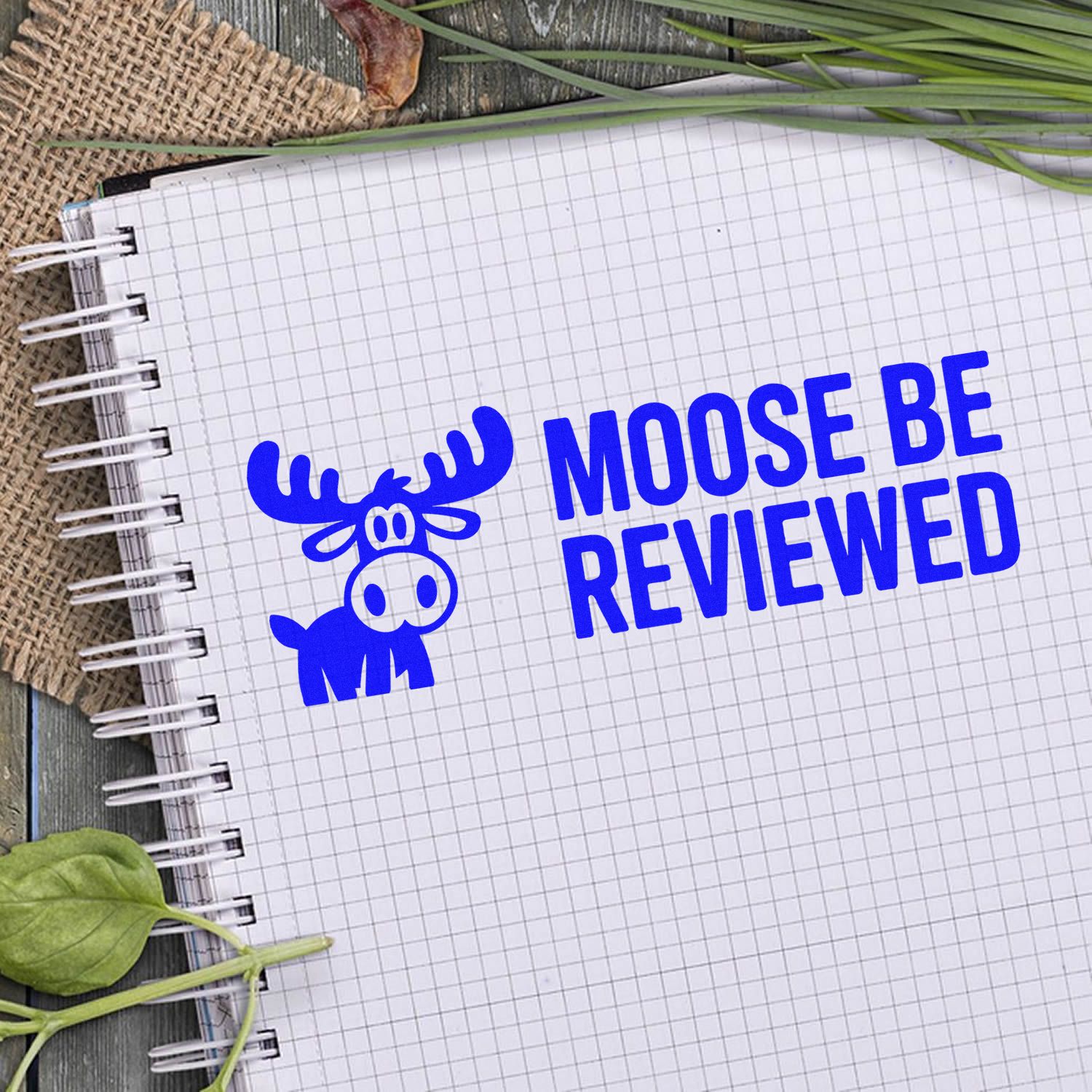 Blue moose stamp and seal with Moose Be Reviewed on a white grid notebook.