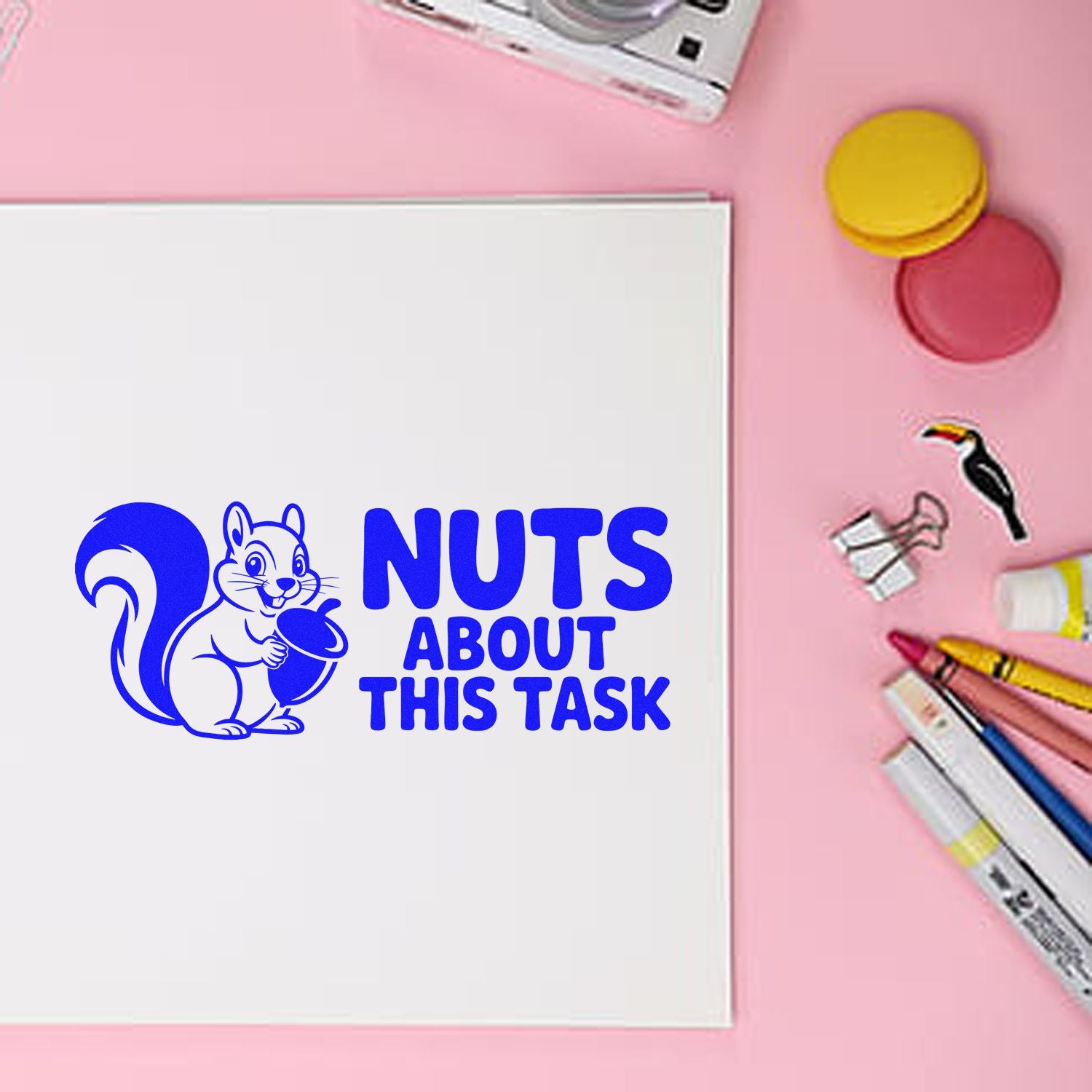 Blue squirrel stamp and seal design on white paper, with Nuts About This Task, pink background and markers.