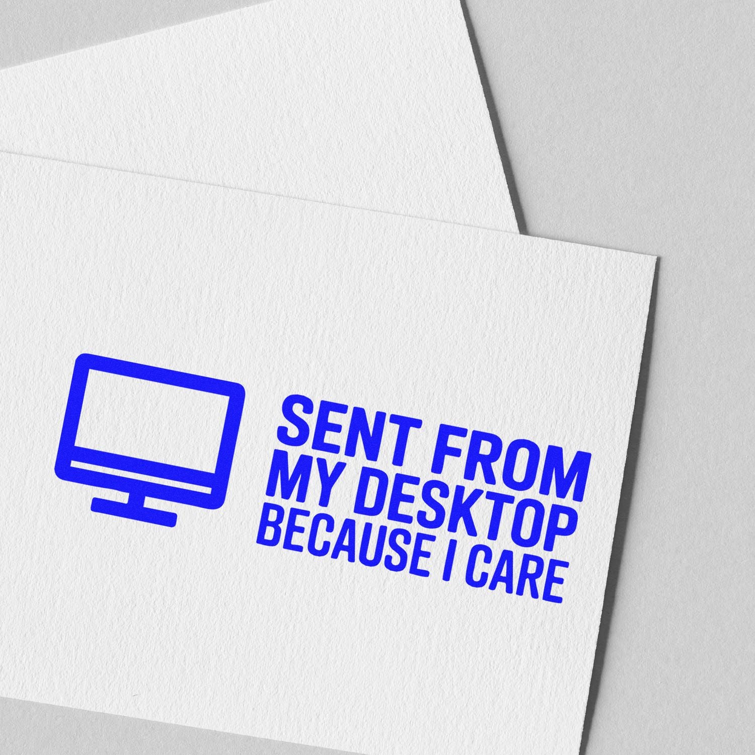 Blue custom rubber stamp and seal with monitor icon and 'SENT FROM MY DESKTOP BECAUSE I CARE' on white textured paper
