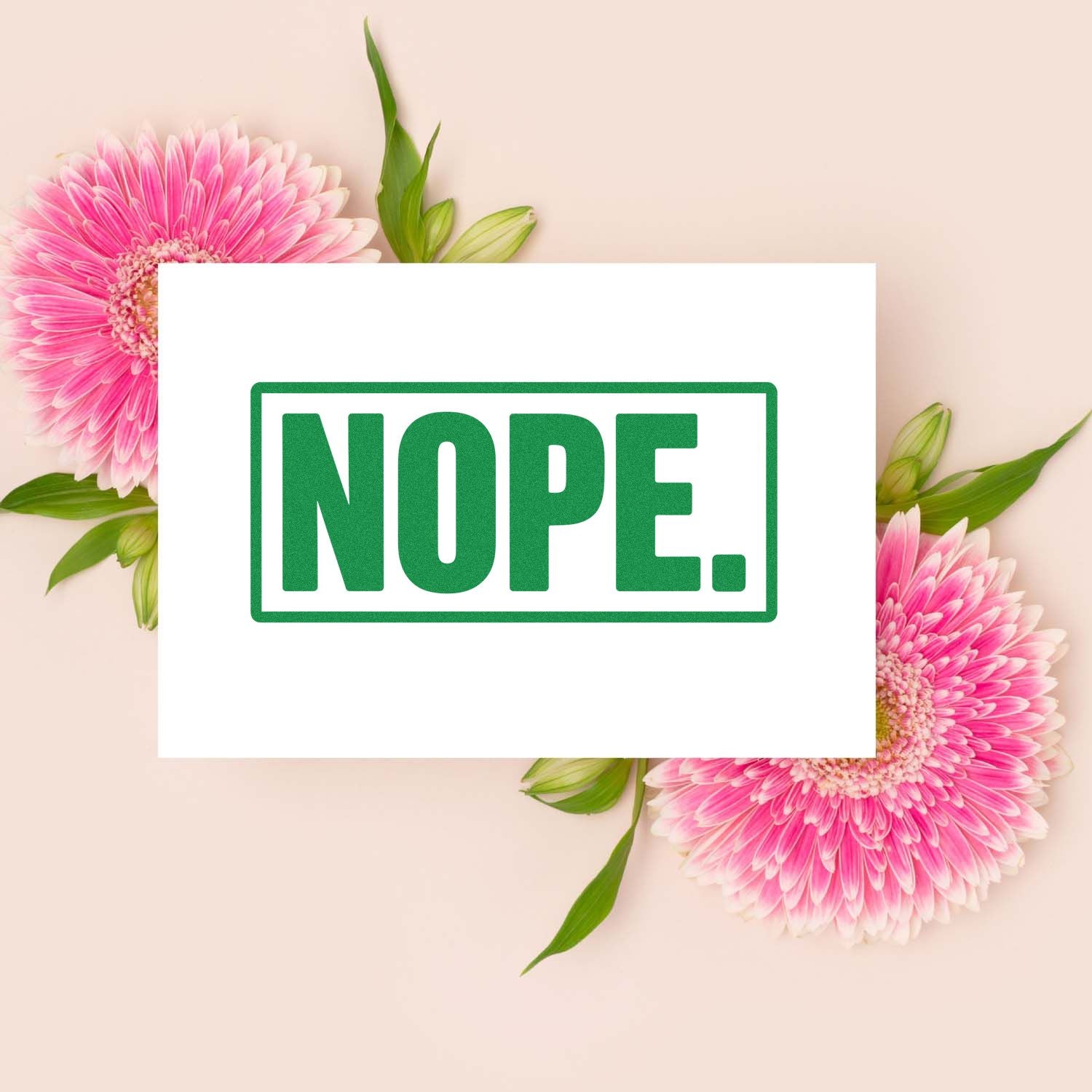 Green NOPE rubber stamp seal on a white card, framed by pink gerbera flowers on a soft blush background.