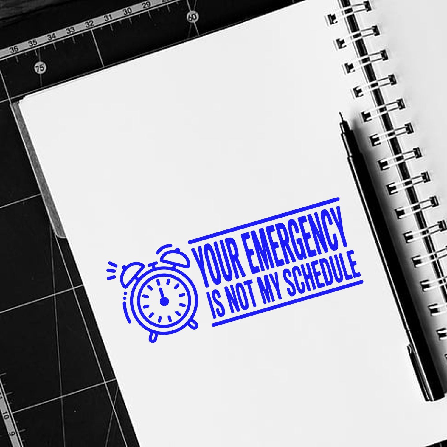 Blue self-inking stamp design with alarm clock icon and Your emergency is not my schedule on a white notebook page.