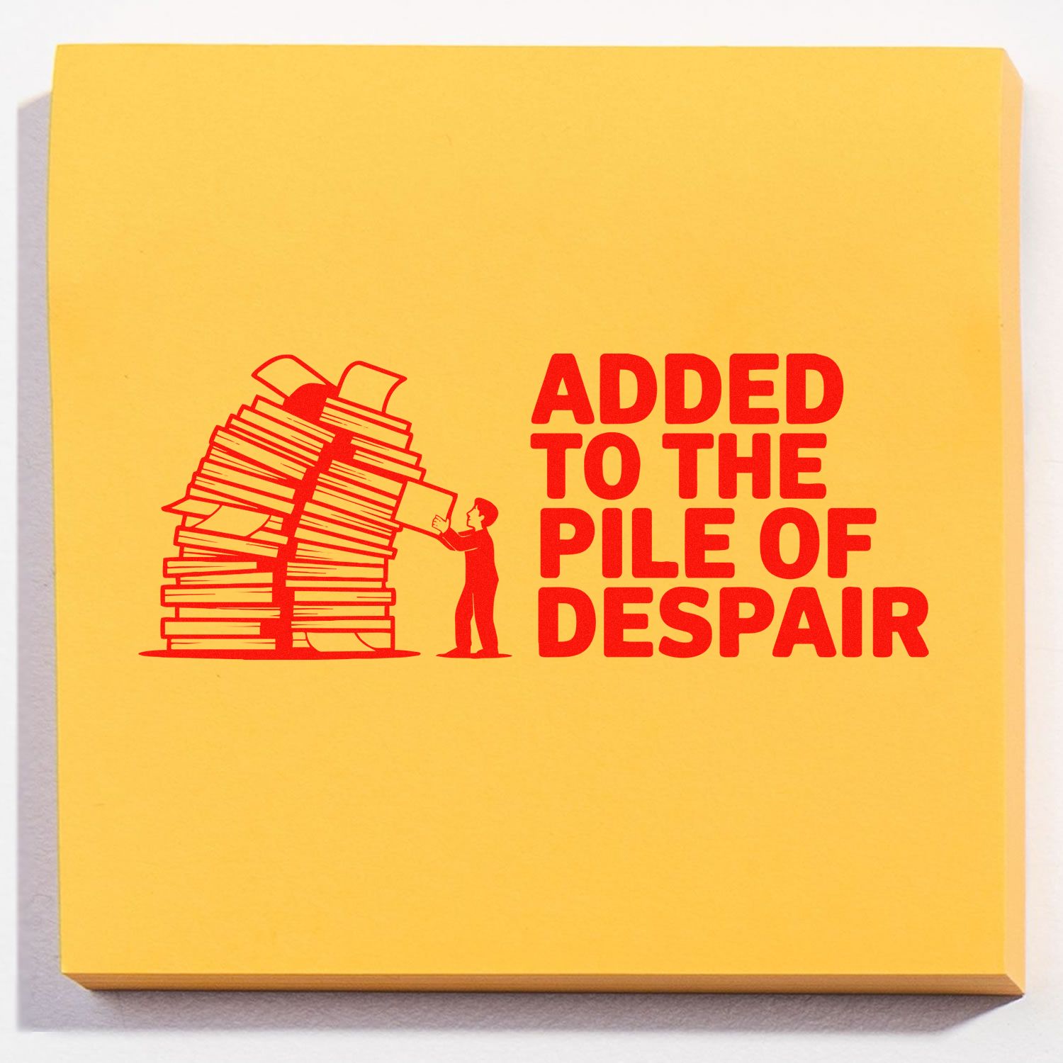 Yellow stamp and seal pad with red stack-of-books graphic and ADDED TO THE PILE OF DESPAIR text.