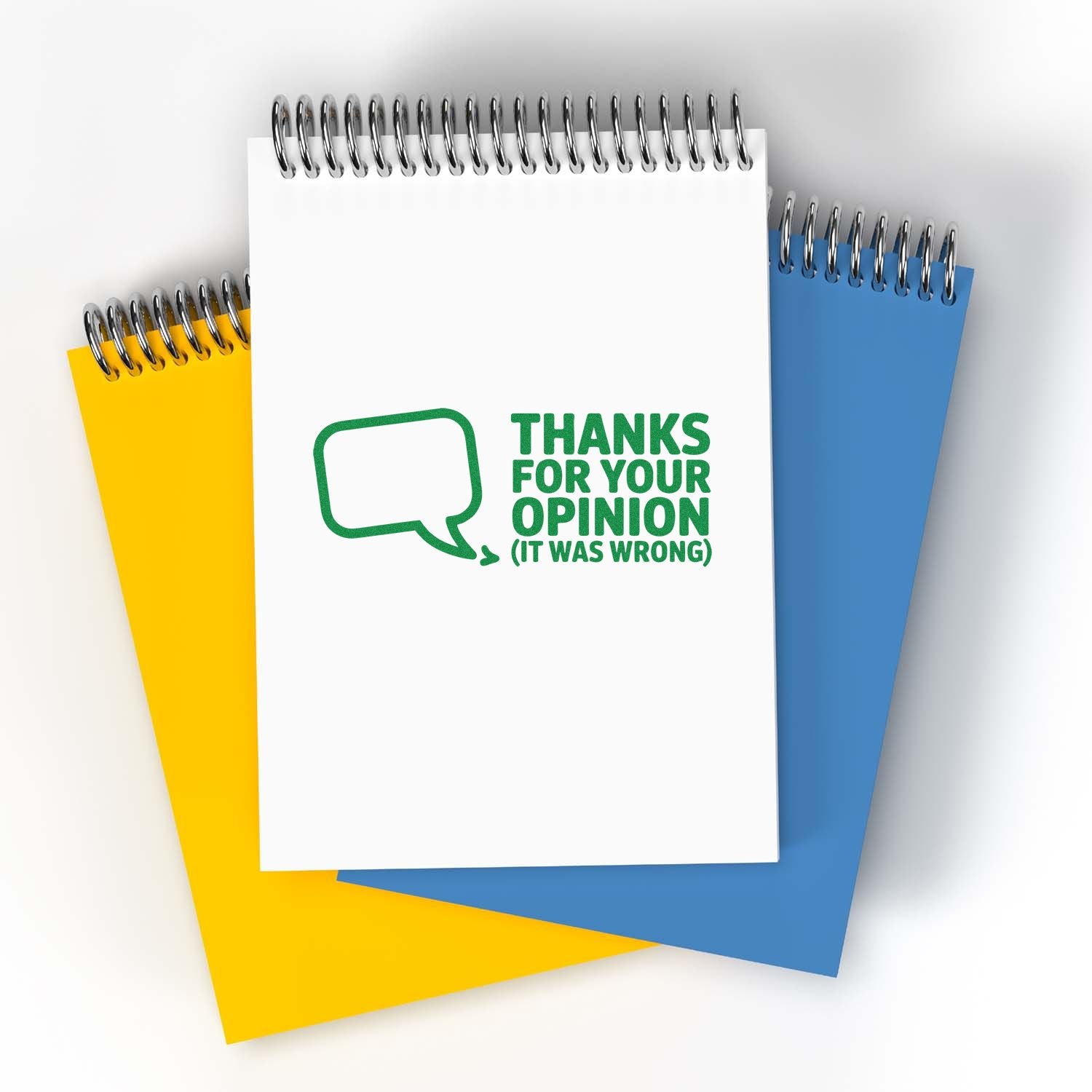 Spiral notepads with green stamp reading Thanks for your opinion (it was wrong), on white, yellow and blue covers.